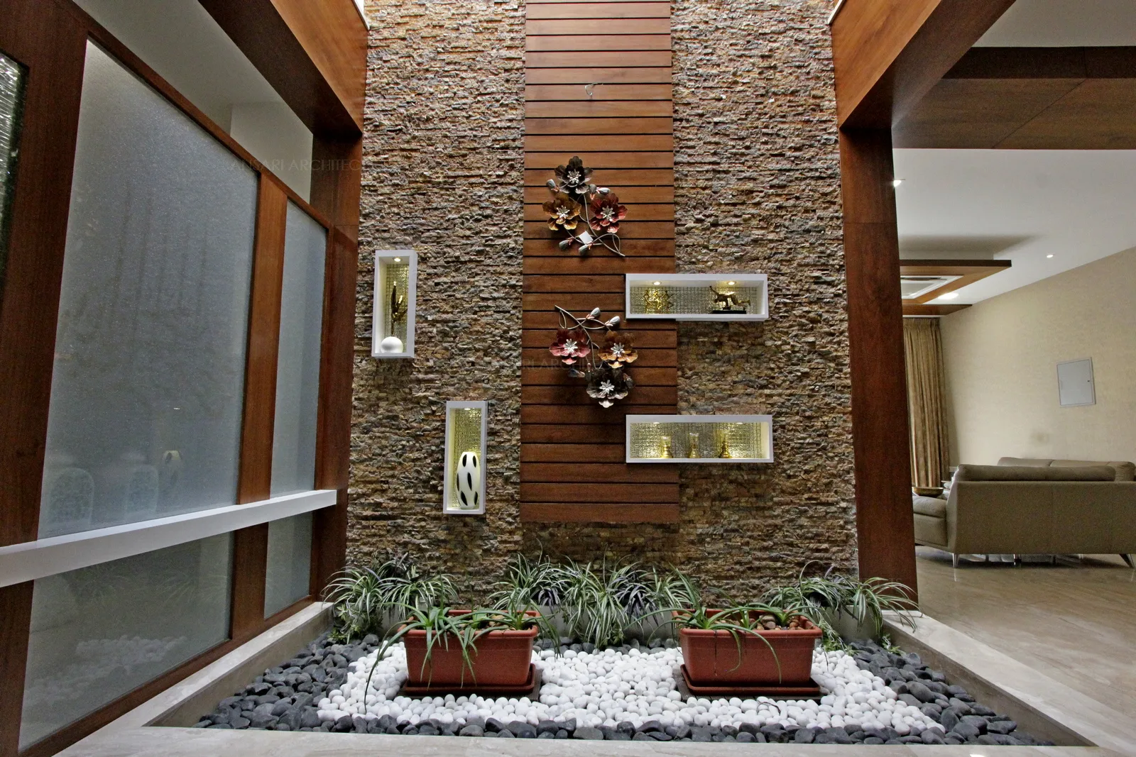 Courtyard is a play of different textures, wood cladding , pebbles, greeneries, glass and stone textures creates a visual connectivity, the niches are arranged to bring a sense of composure to the space with chosen artifacts.