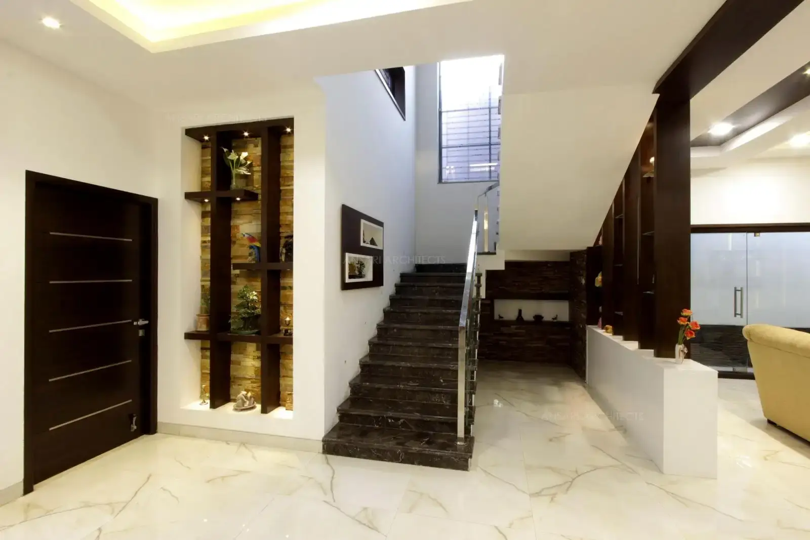 A richly layered decor elements stack the space, the large niche recession with inlay of stone texture and wooden battens adds character to the design at every level. It looks like an emblematic feature here for the entire space.

