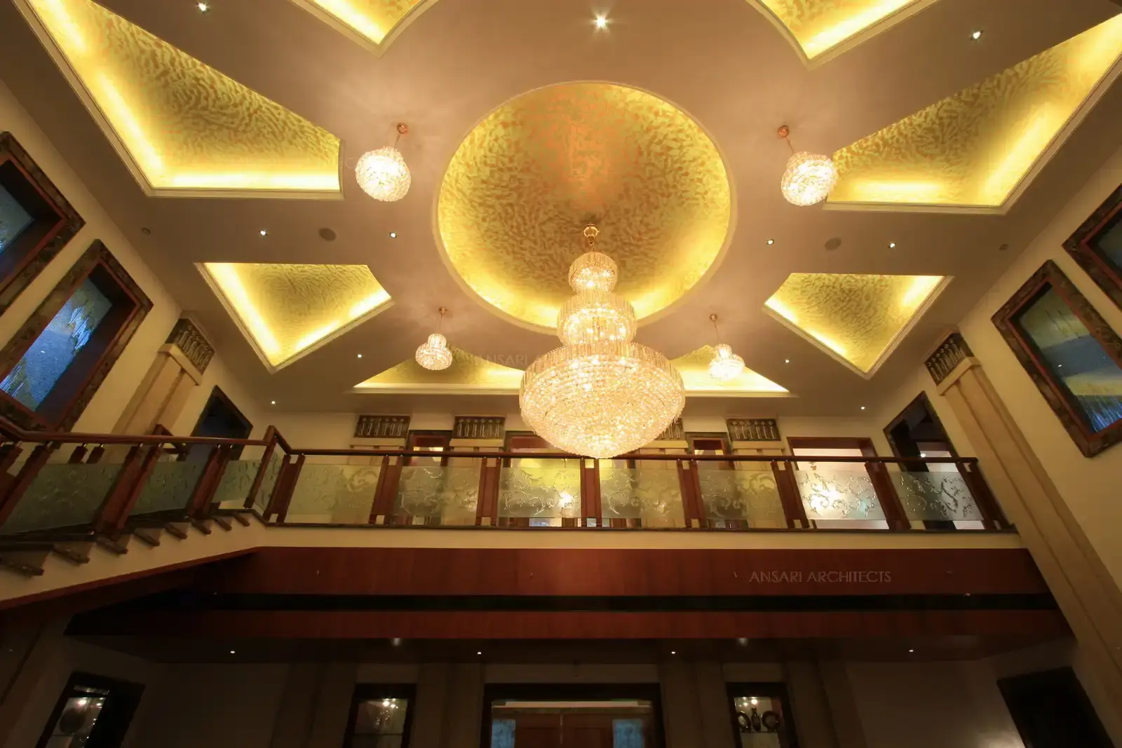 Double height ceiling in the living area is designed in geometric pattern false ceiling with gold foil effect and chandliers for a magnificent look.