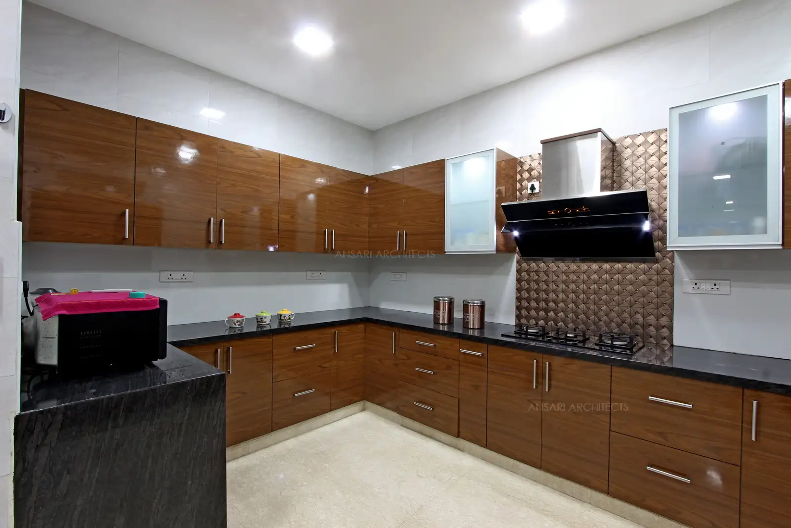 Modular kitchen with laminate finish comprising multiple units with hidden lights under overhead cabinets, wall tiles serve as a backsplash and the kitchen layout looks comprehensive and modish.
