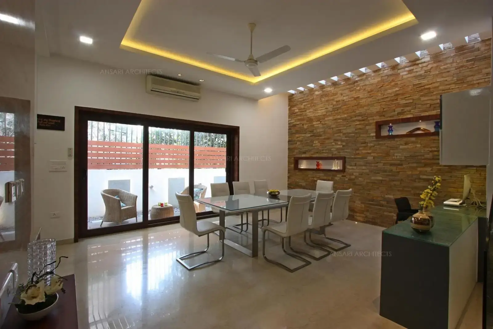 The subtle distinction between the spaces is created by the table used as a decor. The stone textured wall acts as a focal point for the entire space, Niches add primary focus to the wall with lights which enseemingly create a attraction to the artistry. The skylight on the head for the wall creates an abstraction. The large opening with glass door passes in a lots of natural light.