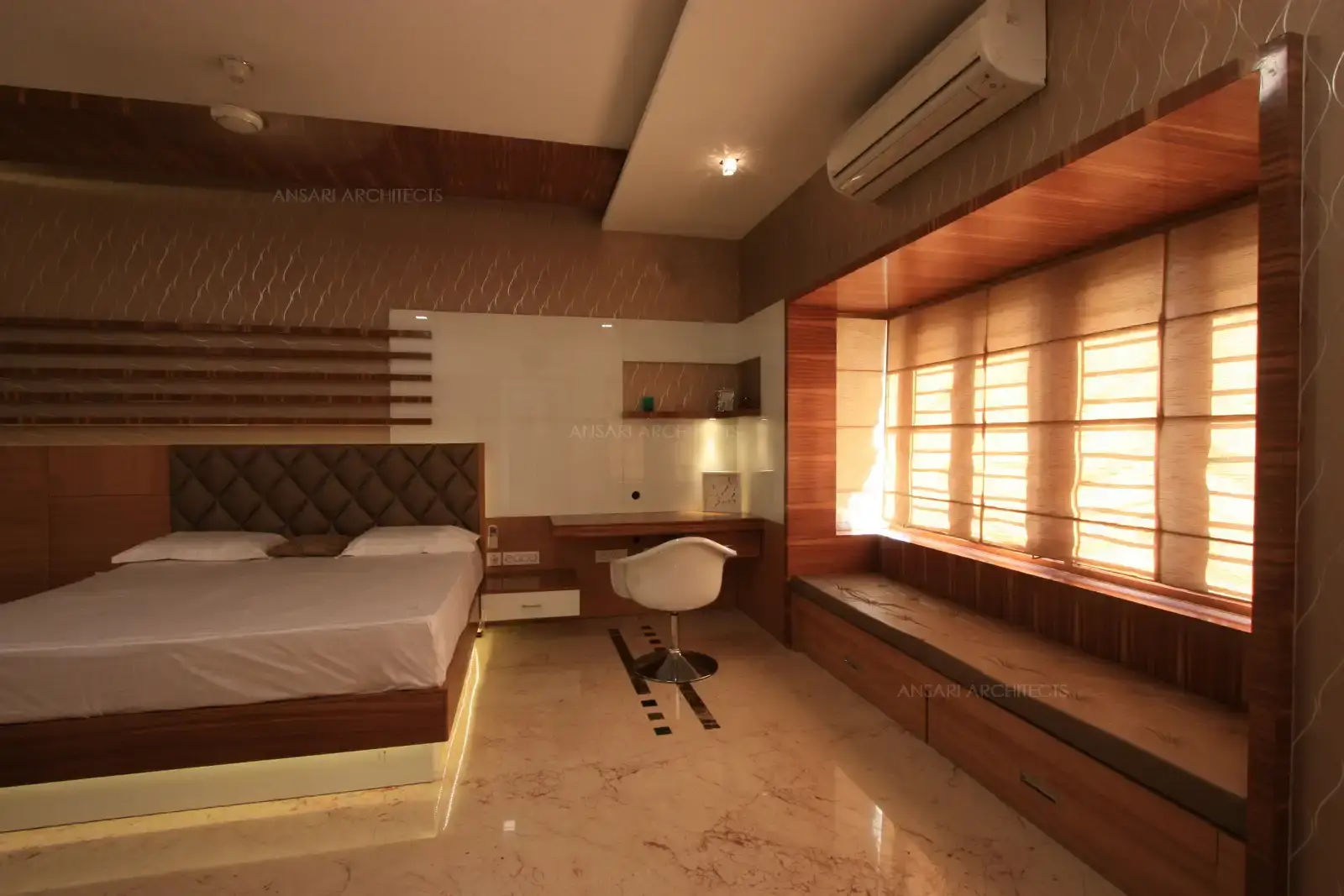 The master bedroom has a neatly placed functional study table and a cushioned seating provided on the modern bay window.
