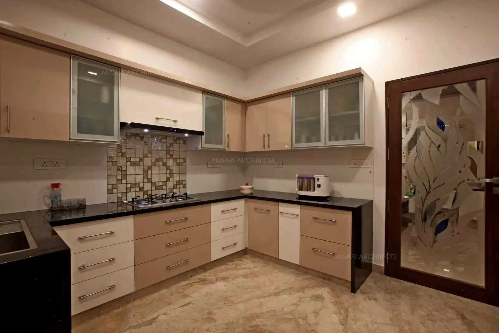 All clutter is hidden inside the cabinets , the look of fresh white cabinets and burst colour provided by the backdrop tiles with deliberate pattern near the hood. Hidden lights and lite tones add to the space. Sleek cupboards all equal sizes arranged in symmetry for storage. All small details add upto an harmonious whole space.
