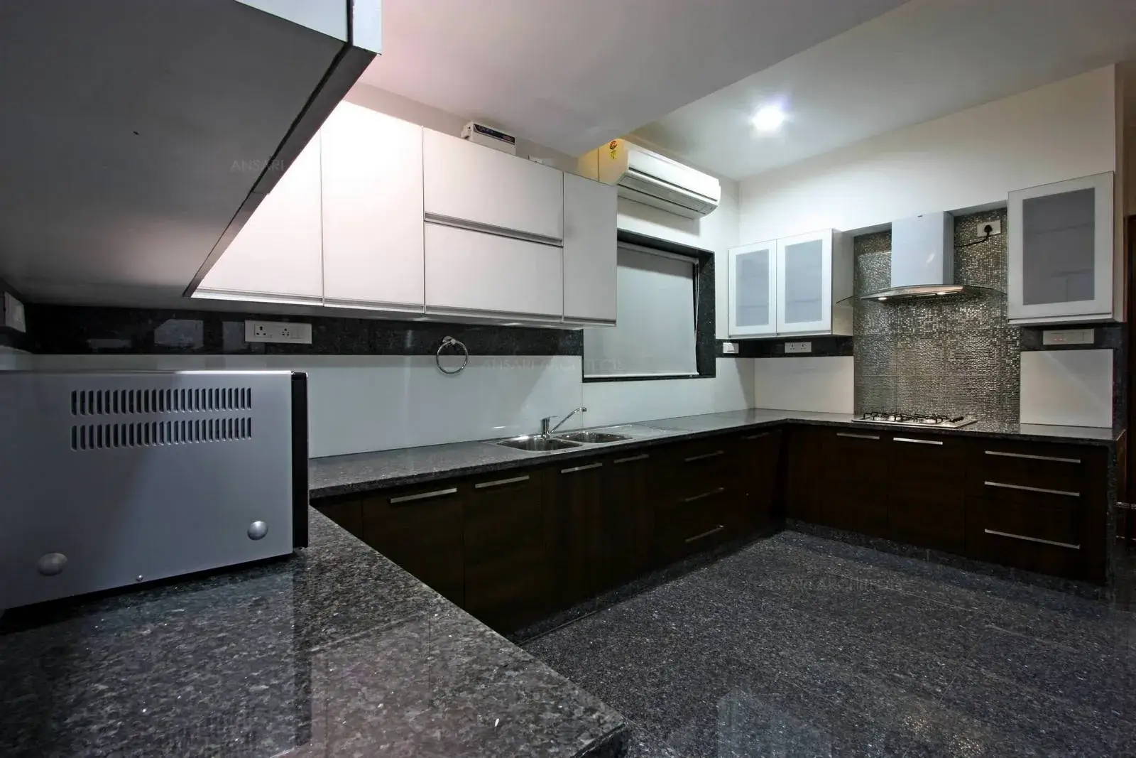 Kitchen is designed with neutral colour scheme three fold modular unit with granite finishes and storage cabinets above and artificial lights are provided for the space.