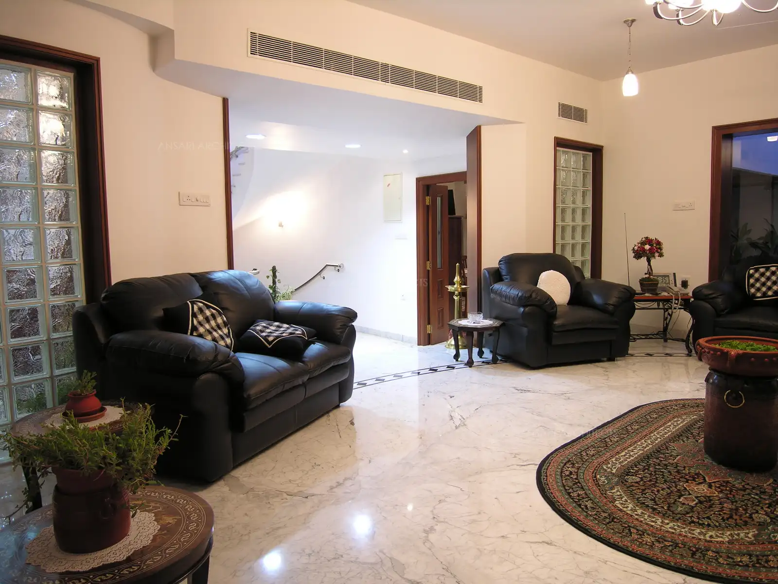 The entrance to the living room is flanked by black leather, sofas and glass brick walls. The air conditioning is centralised through the ducts.
