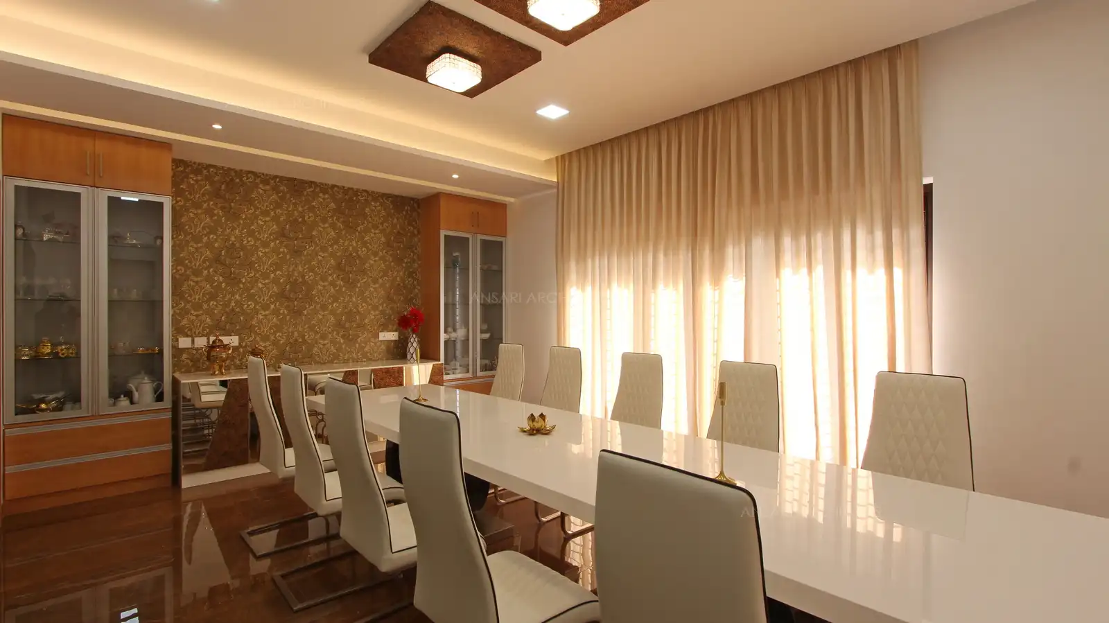 The dining space is set in all white, complemented by dark floor and white furnitures, gets a punch of style with the ceiling studed bright lights. Large windows ensure that the room is weel lit to counter the all bleached palette.