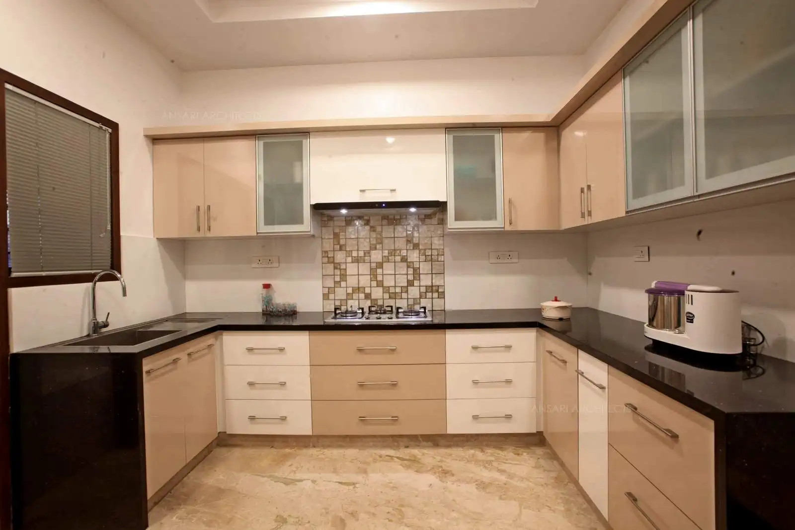 The contemporary colour pallette of the kitchen is peach and white. The counter runs three- sided for the kitchen allowing for optimum usage for a clear workspace. The shades transform the entire zone into a picturesque corner. The marble floors add to subtle depth of the room.