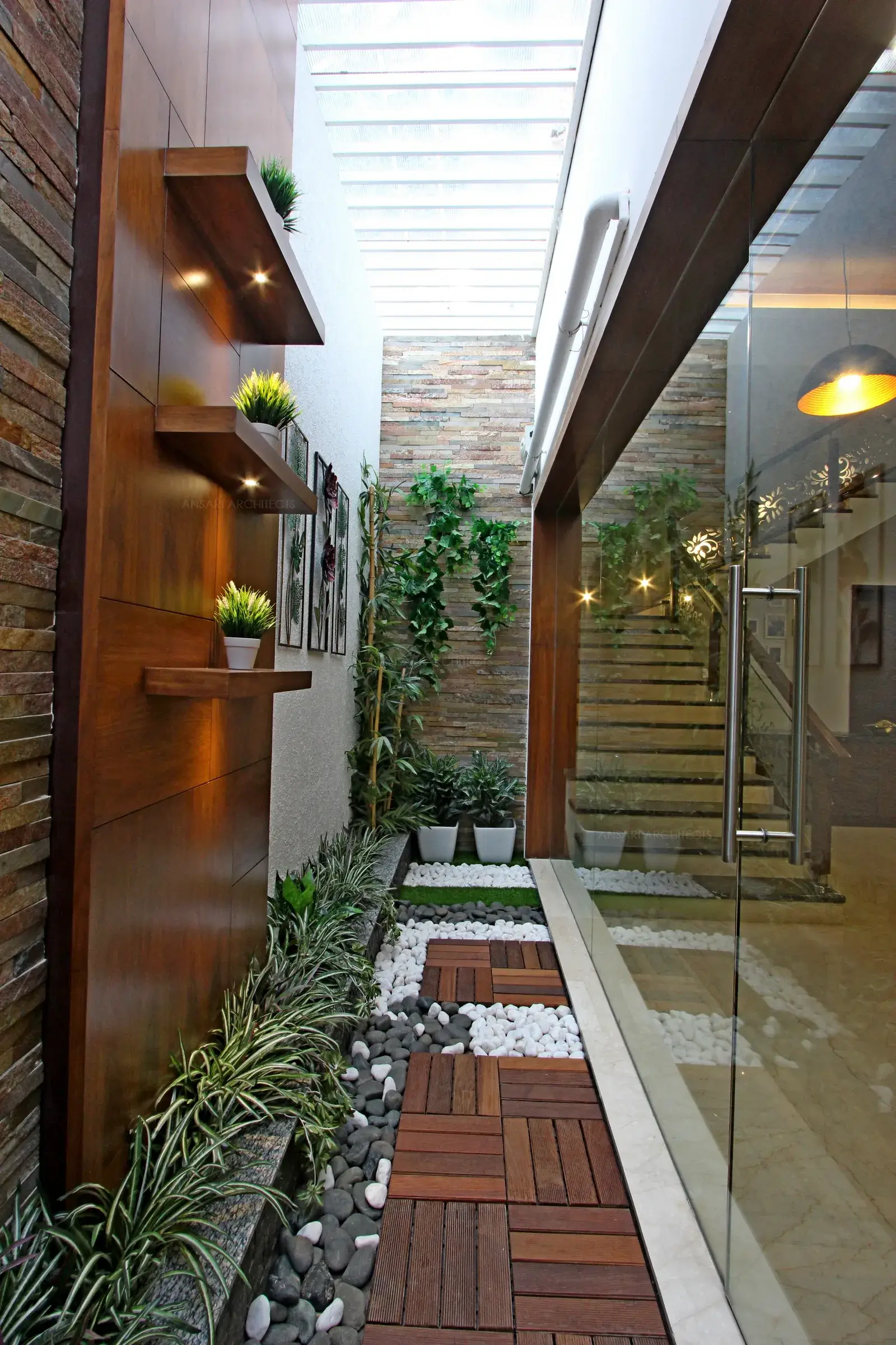 The Courtyard acts as a feature for bringing in natural light, with dark-toned wooden battens that enclose the flooring with the pebbled zone. Large Glass allows uninterrupted views. The plants add a touch of softness featuring a miniature rock garden.