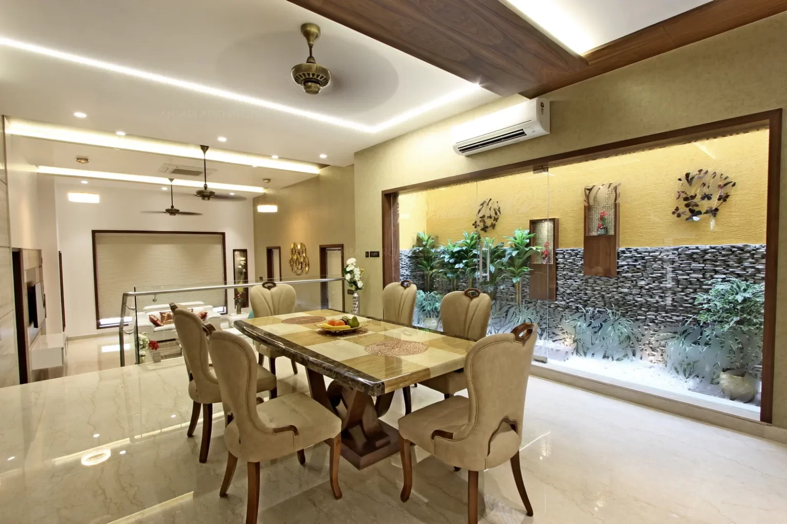 The dining area remains well connected to the living area in a raised platform and the space overlooks the courtyard. The levels create a mode of enthusiasm for the space. The furniture is a traditional decor element.The brown amd cream tones have lighter hues and hence provides warmth.