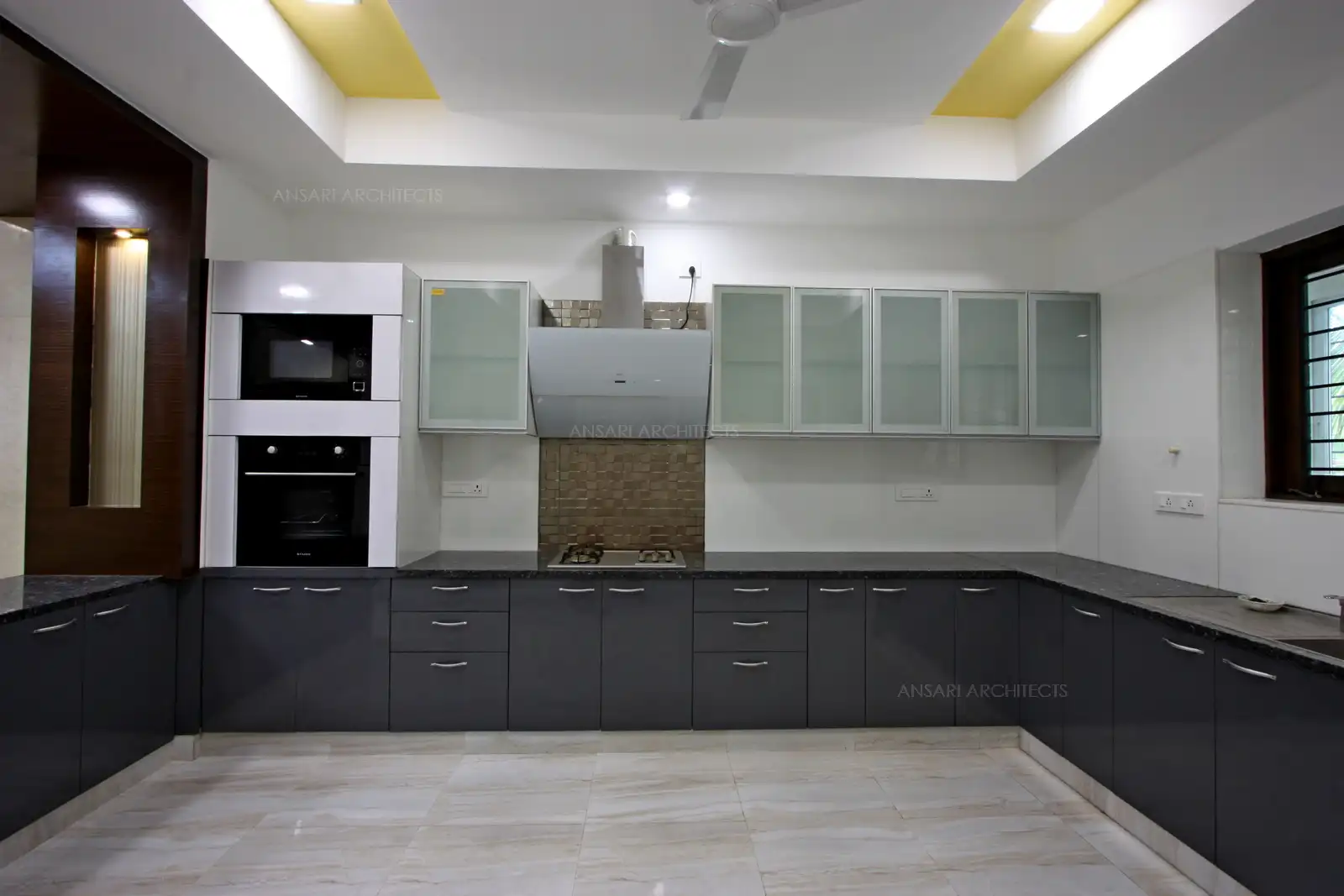 An elegant modular kitchen with touch of dark wood panelling for niches and artificial lights brighten up the space.