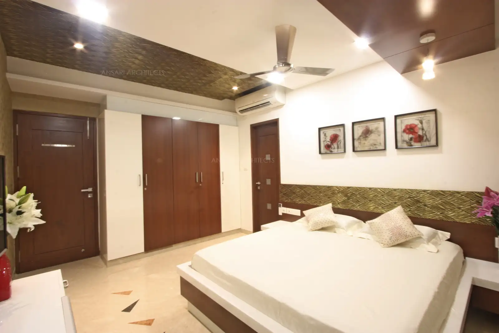A royal splendour of golden printed wallpaper makes a stunning design, the theme is extended by wood finish bed and warm sconces of light framing the space. The window provides a majestic look.