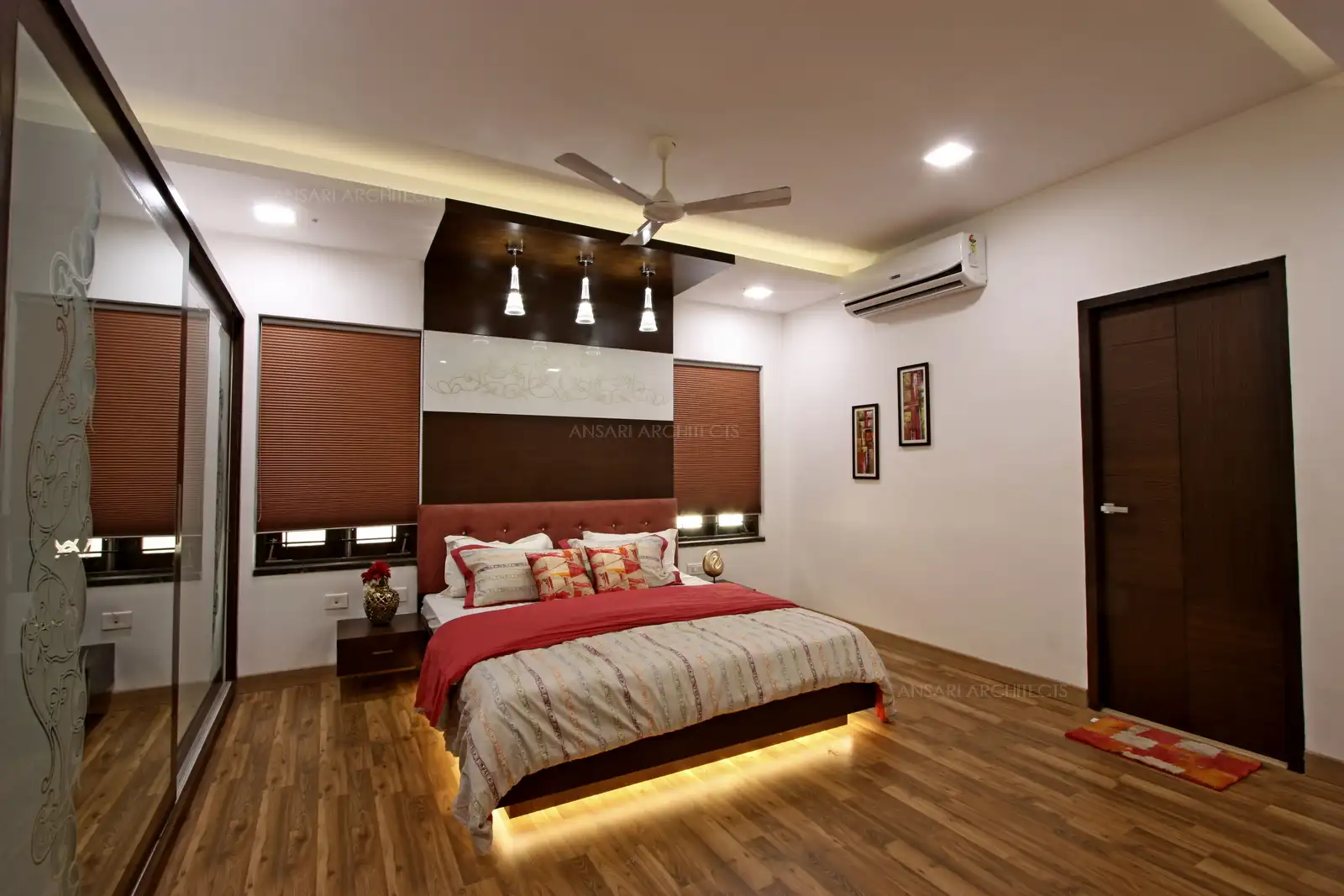 Hanging spot lights and wooden textured flooring gives a vibrant appeal to the space along with the false ceiling and the window on either sides of the bedroom that welcomes natural light provides a modern look for the bedroom.
