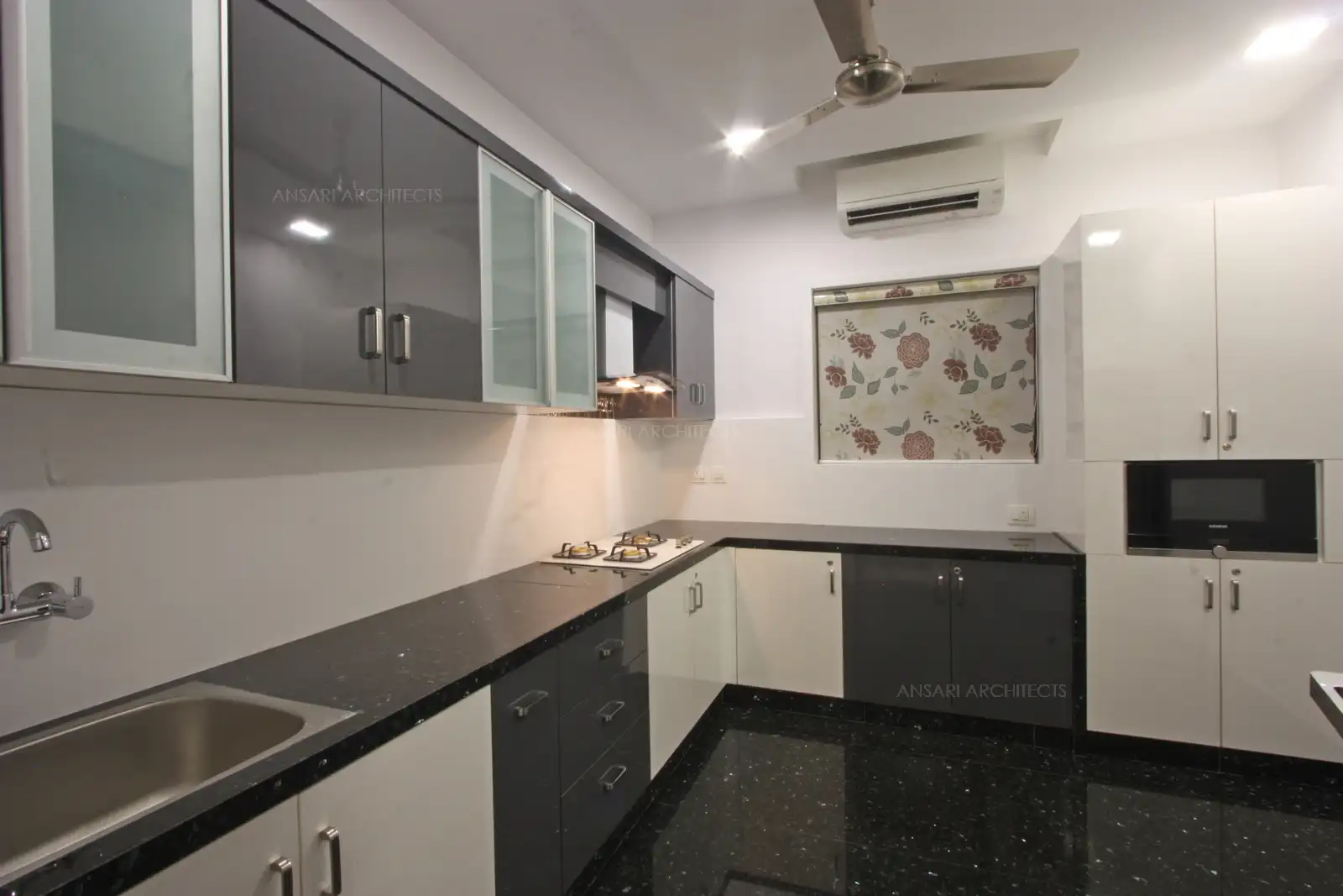 The well planned kitchen packs a conventional layout, grnaite- topped counter, colour scheme looks neutral with more white to make it spacious. The floating cabinets attached to walls, sleek cabinets and ambient lights line the ceiling.