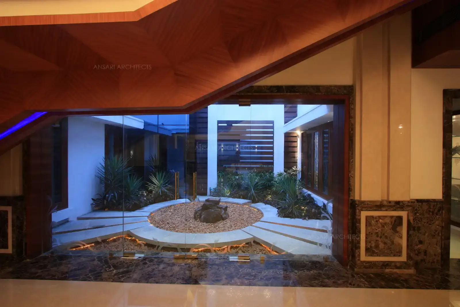 Landscaped courtyard is designed in rough stone finish and wooden penels on the wall along with few natural shrubs.