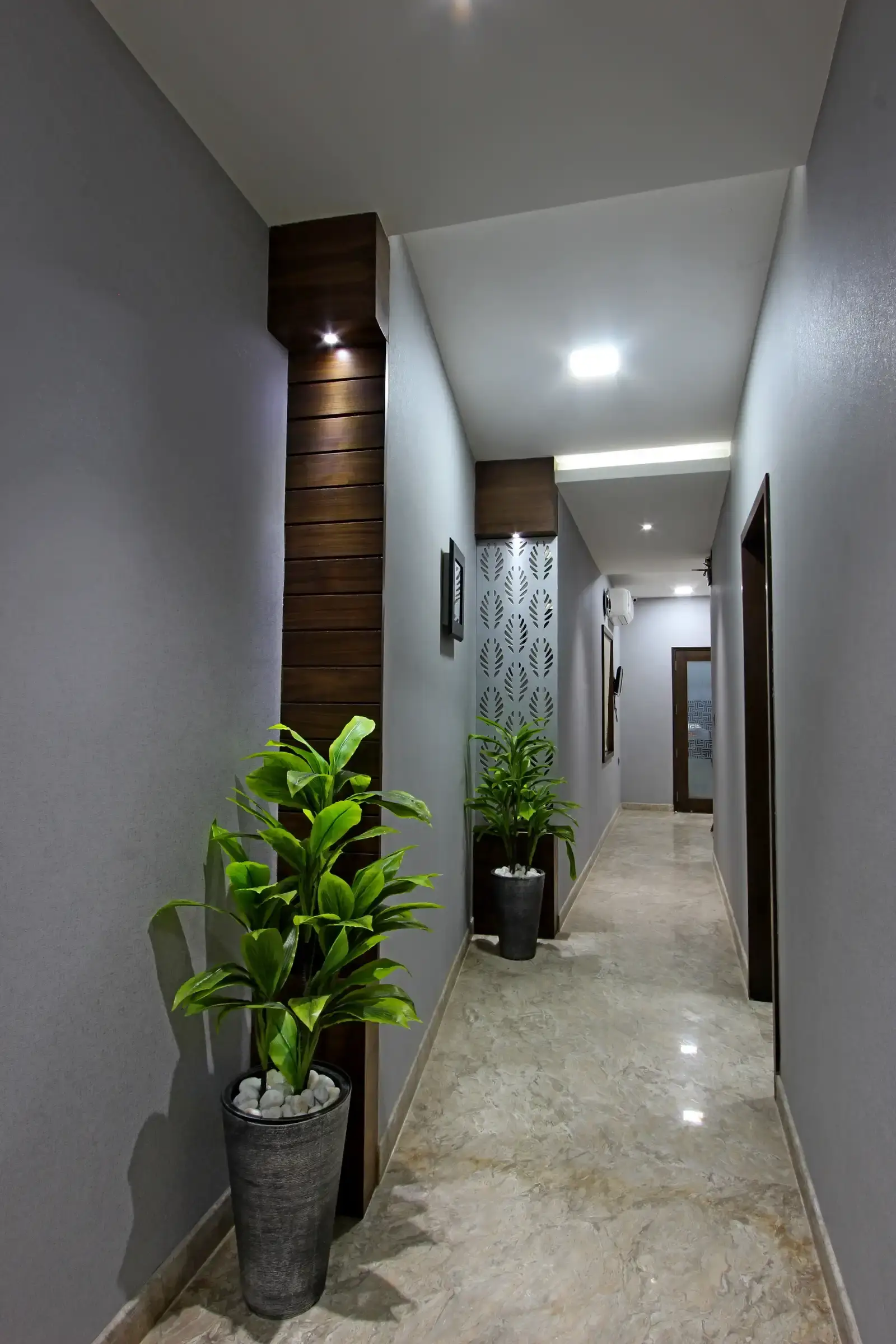 The passage way is innovatively designed with plush green plants that layer natural colour along with rustic pots and the wooden panelling with recessed lights .