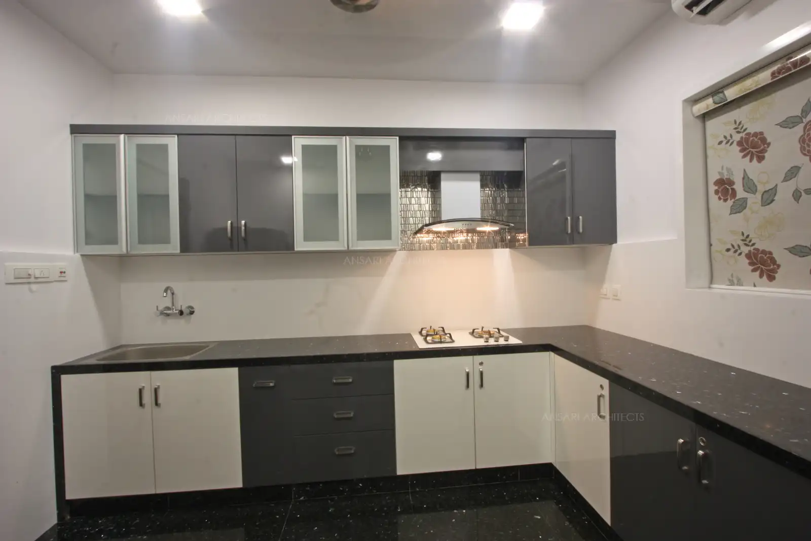 The light bounces off the glossy cabinets, play of contrasts yet a uncluttered space with clean cabinets for a streamlined look. The backsplash pattern behind the hood suits the theme of the kitchen.