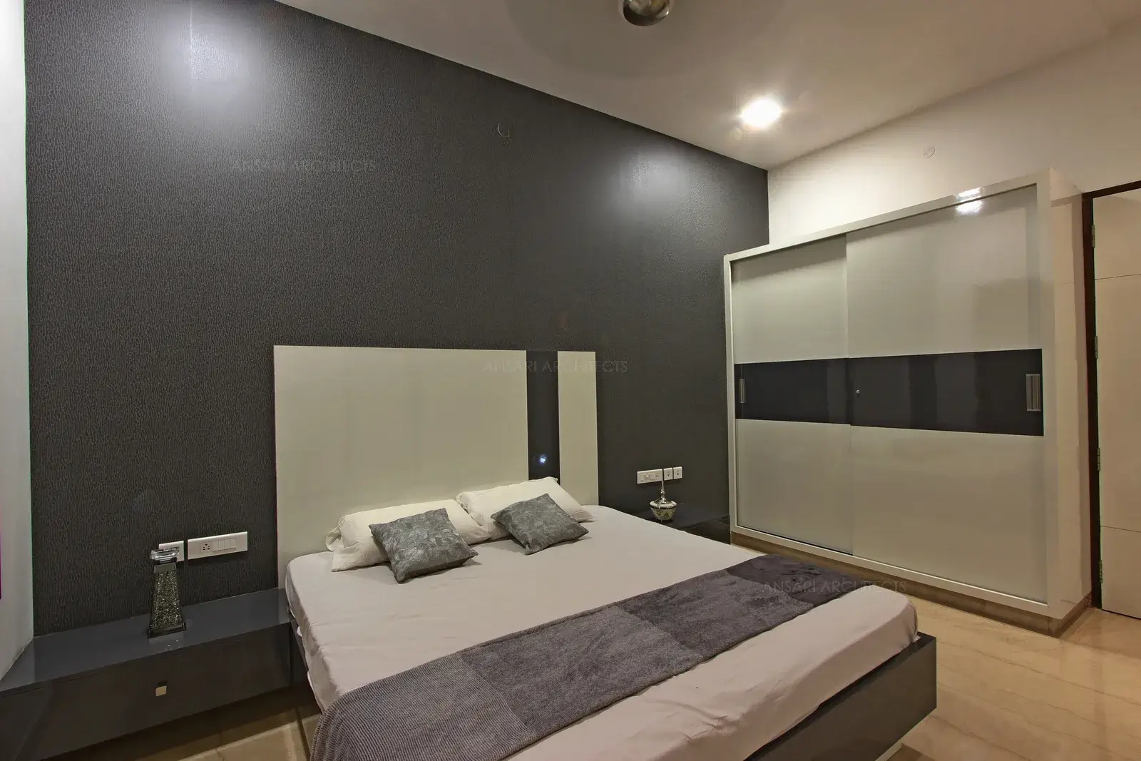 Master bedroom with contemporary retreat, with muted grey tones, walls accentuated with grey textured wallpaper with headboard design is simple. Wardrobe adds extrra pep with grey tone reflected here. Soft vibes replenish the bedroom.