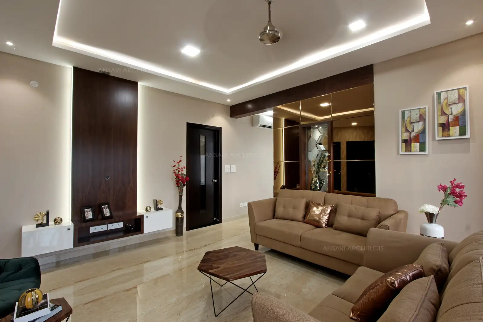 The mirror panelled partition wall merges clean straight lines, beige tone of the cosy sofa, marble flooring accentuated with floral motifs. Ethnic painting takes over the wall behind the sofa.