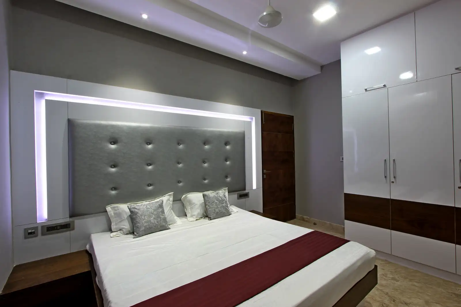 The bedroom with wooden textured flooring and white walls has a relaxed vibe to it. The tall wardrobes with veneer stip detailing enhances the beautyof the space.
