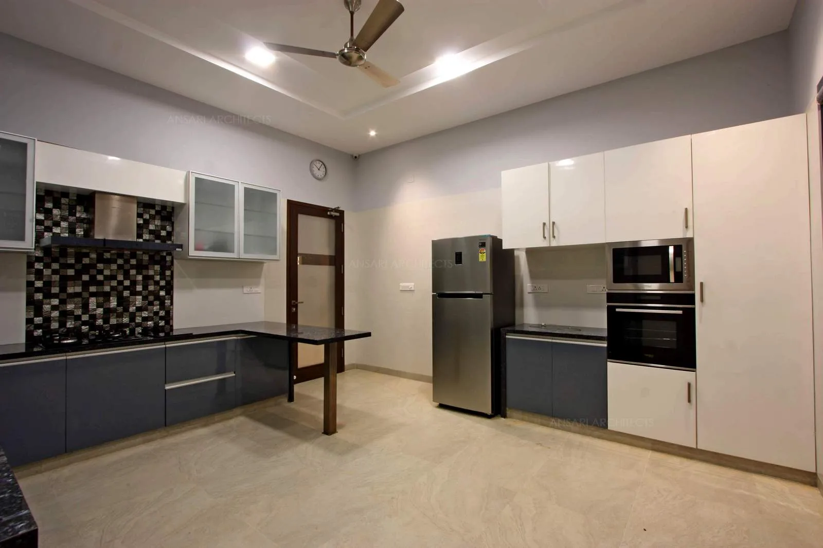 The crisp white setting with cabinets on both sides camoufalges with the wall, neutral coloured kitchen punched with vibrant hues of backdrop tiles. Hidden lights under cabinets and chest of drawers.