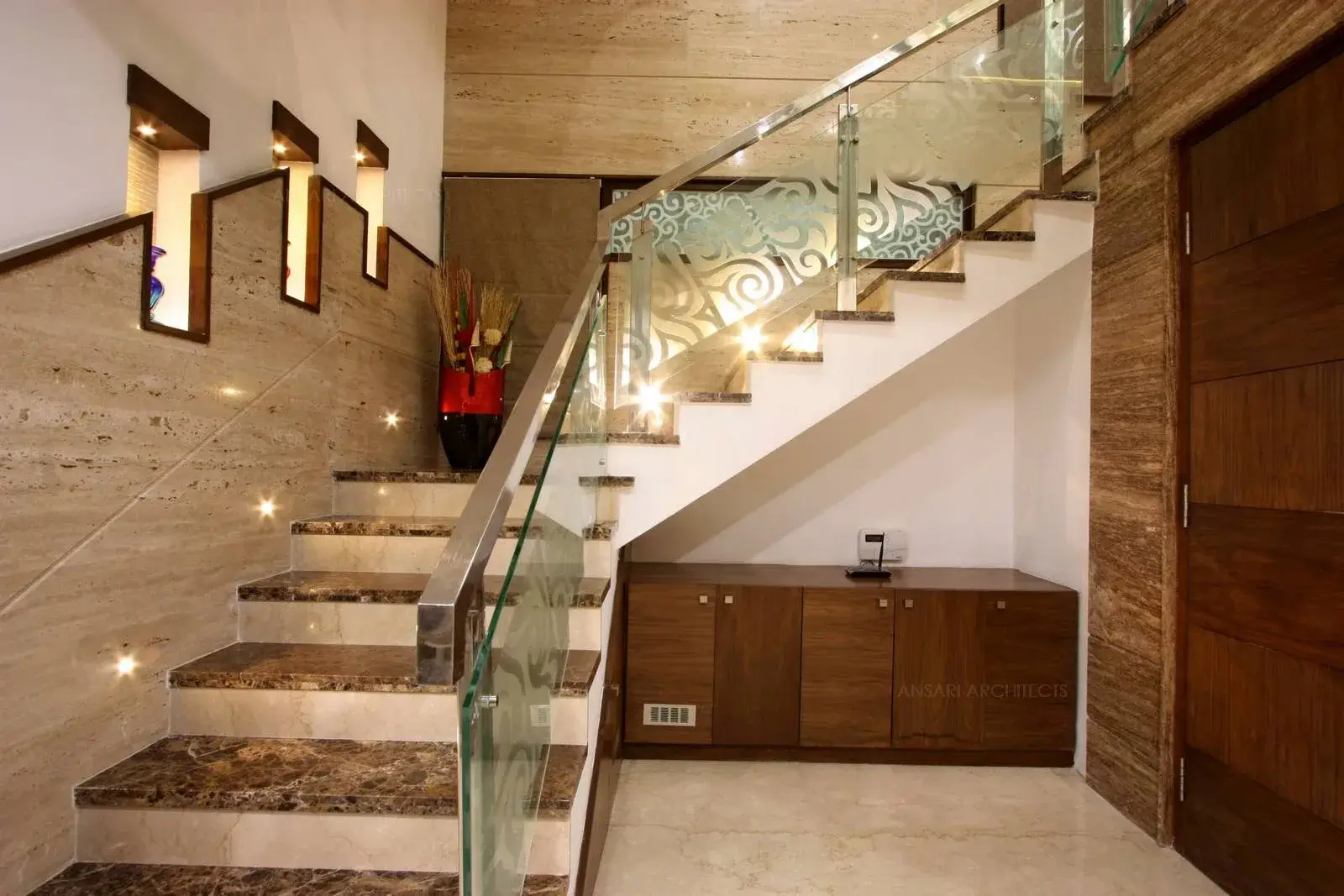 Wall niches are highlighted with lights and the space below the staircase is being functionally used as a storage unit. The entire area is covered with wooden panelling.