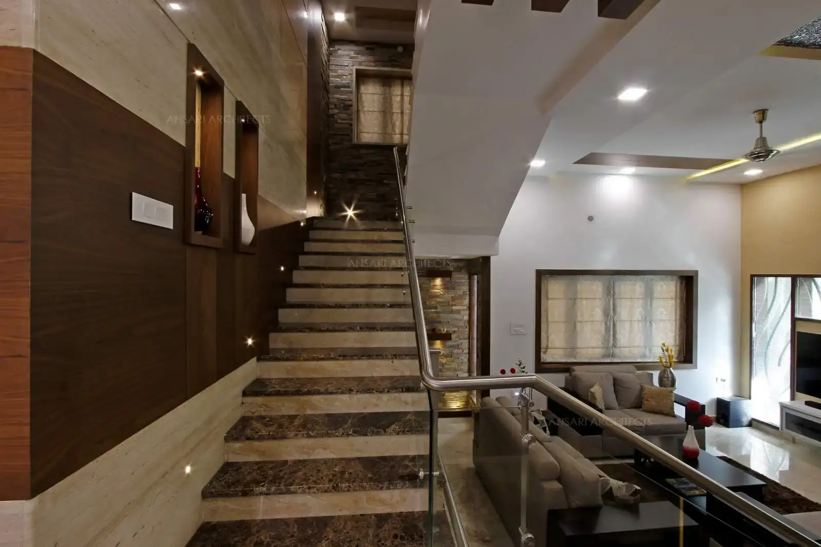 The classic staircase with marble with glass handrails and metal detailing. Veneer niches highlight the walls and the stone texture cladding lends a unique character to the space.