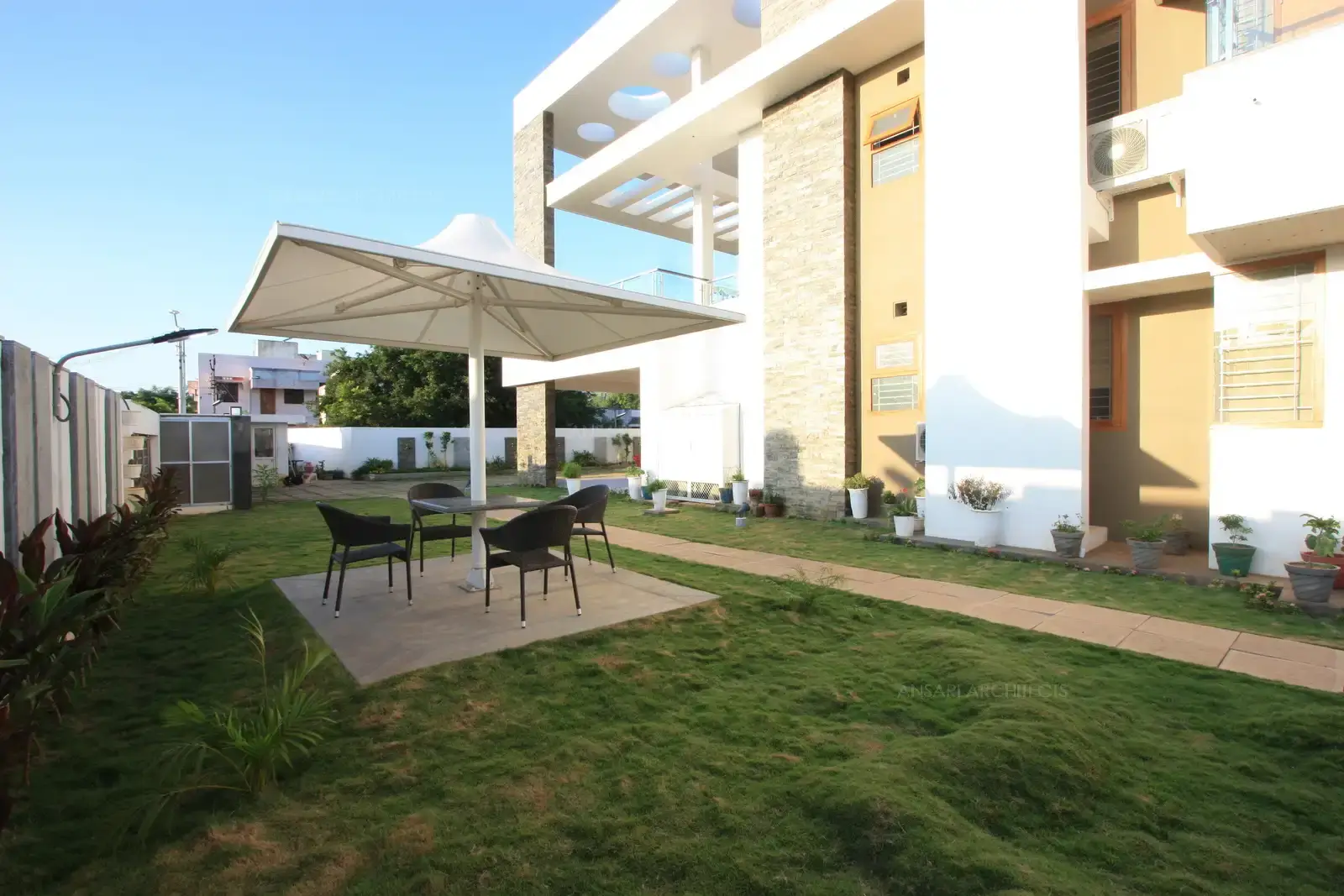 The garden area is provided with seating on a hard flooring surrounded by grass turf and covered with a modern tensile structure.