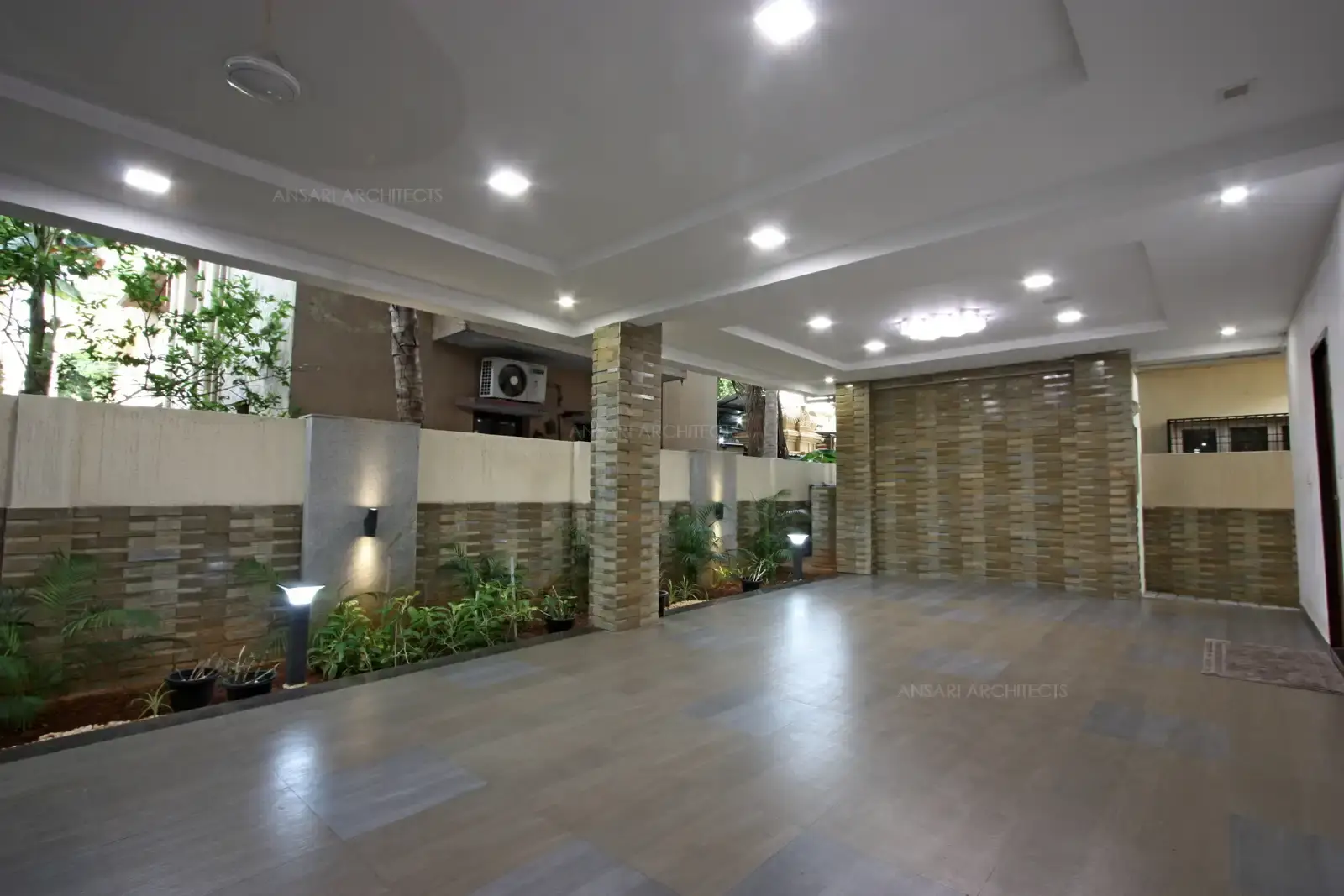 Car porch merging landscapes and stone cladding on walls and contrasting flooring provided with spot lights.