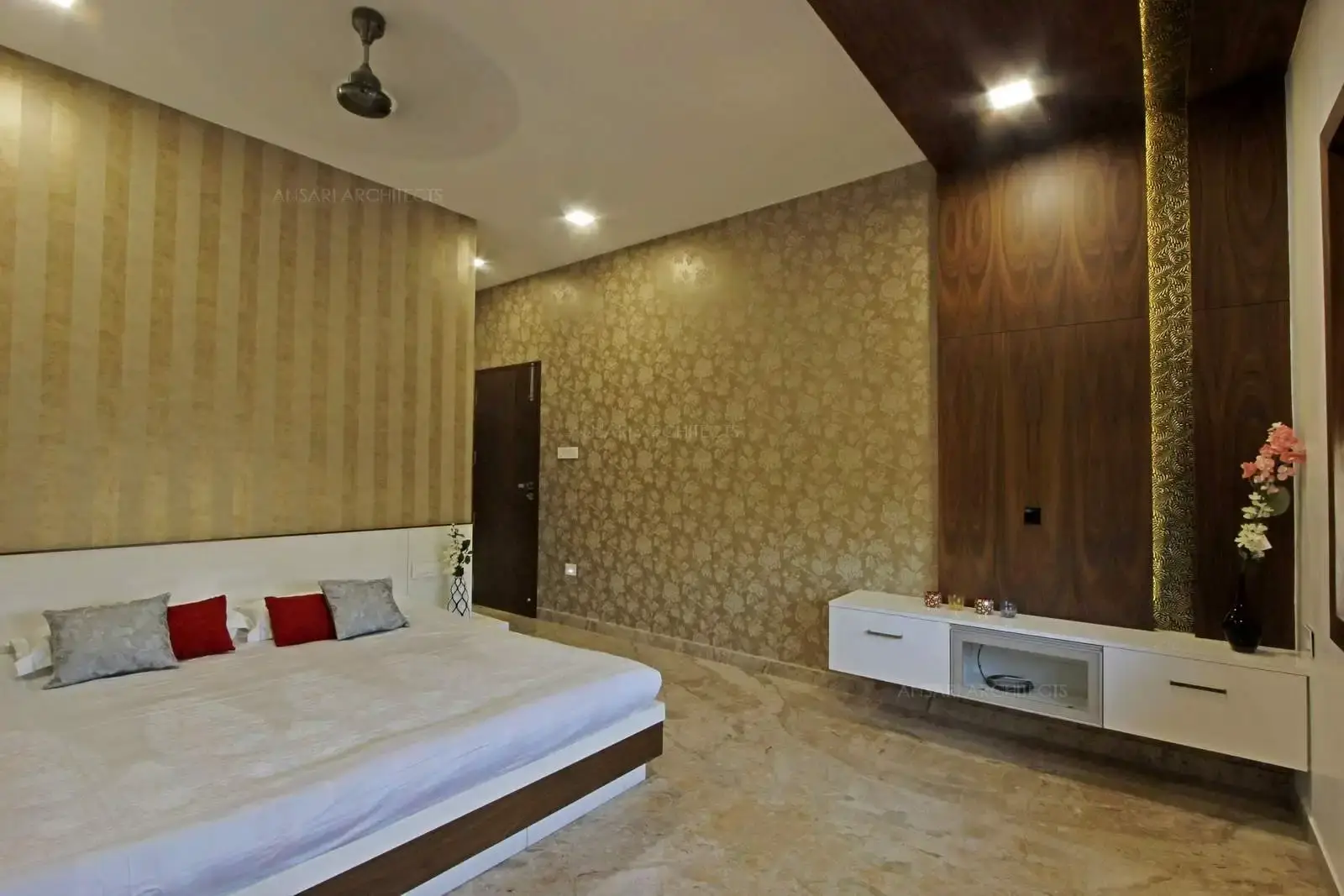 The striking iteration of gold in this bedroom feels eclectic conveying the shades of a bright morning sky. The headboard is effectively serves white and the entire space remains tranquil. The classic wood tones in the wall-ceiling cladding takes to serene space and golden gleams continue all over the walls with different texture patterns. The petite storage unit seamlessly blends with background.