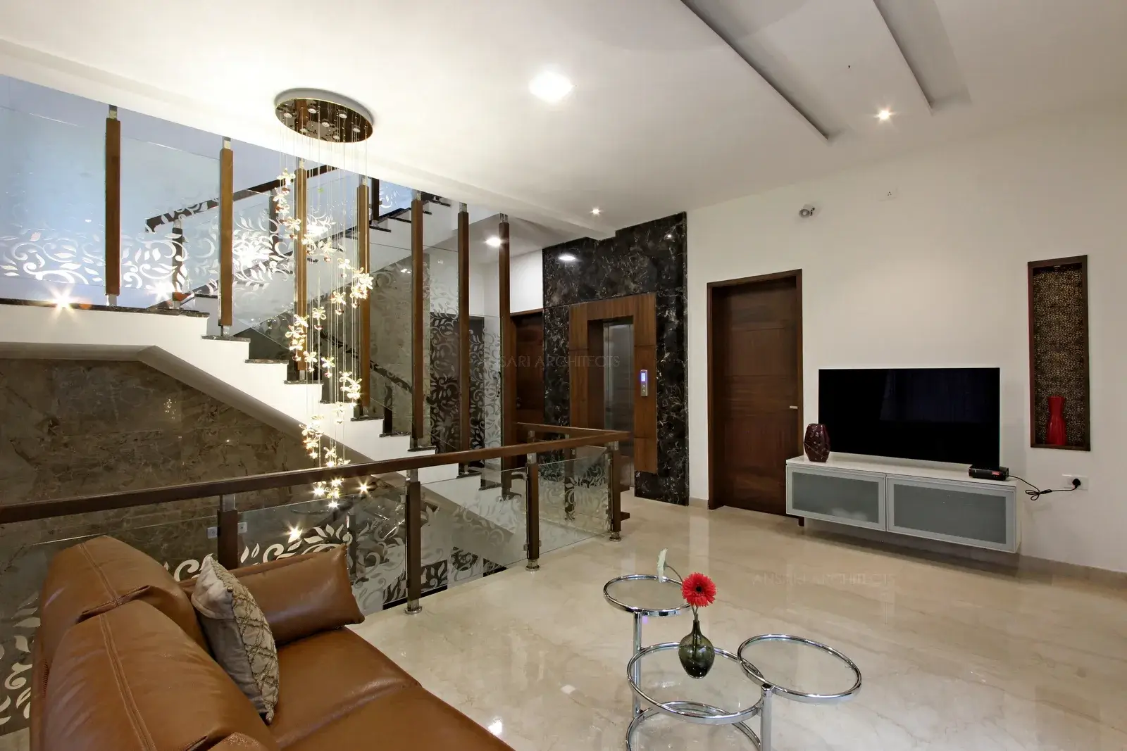 Tv unit looks sleek with niches inlit with golden lining and recessed lights. The functional unit looks uncluttered and clean. Ceiling looks simple, with rectangular strip lights that provide a subtle glow.