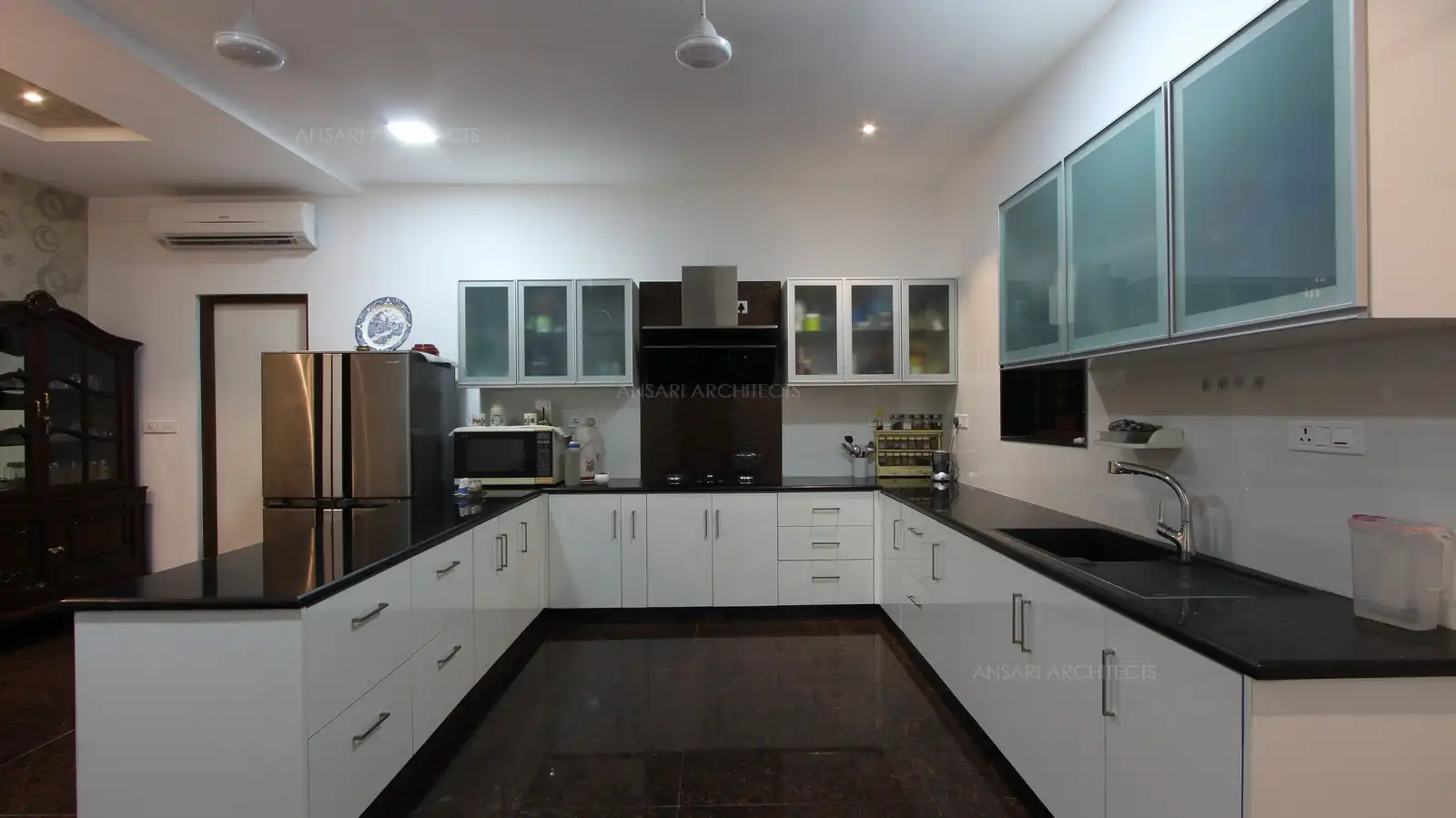 The U shaped counter is a convenient layout balances cabinet with cooking space, spotless and handle free floating cabinets. Neutral coloured kitchen punched in with vibrabt brown hue through patchwork backsplash tiles.