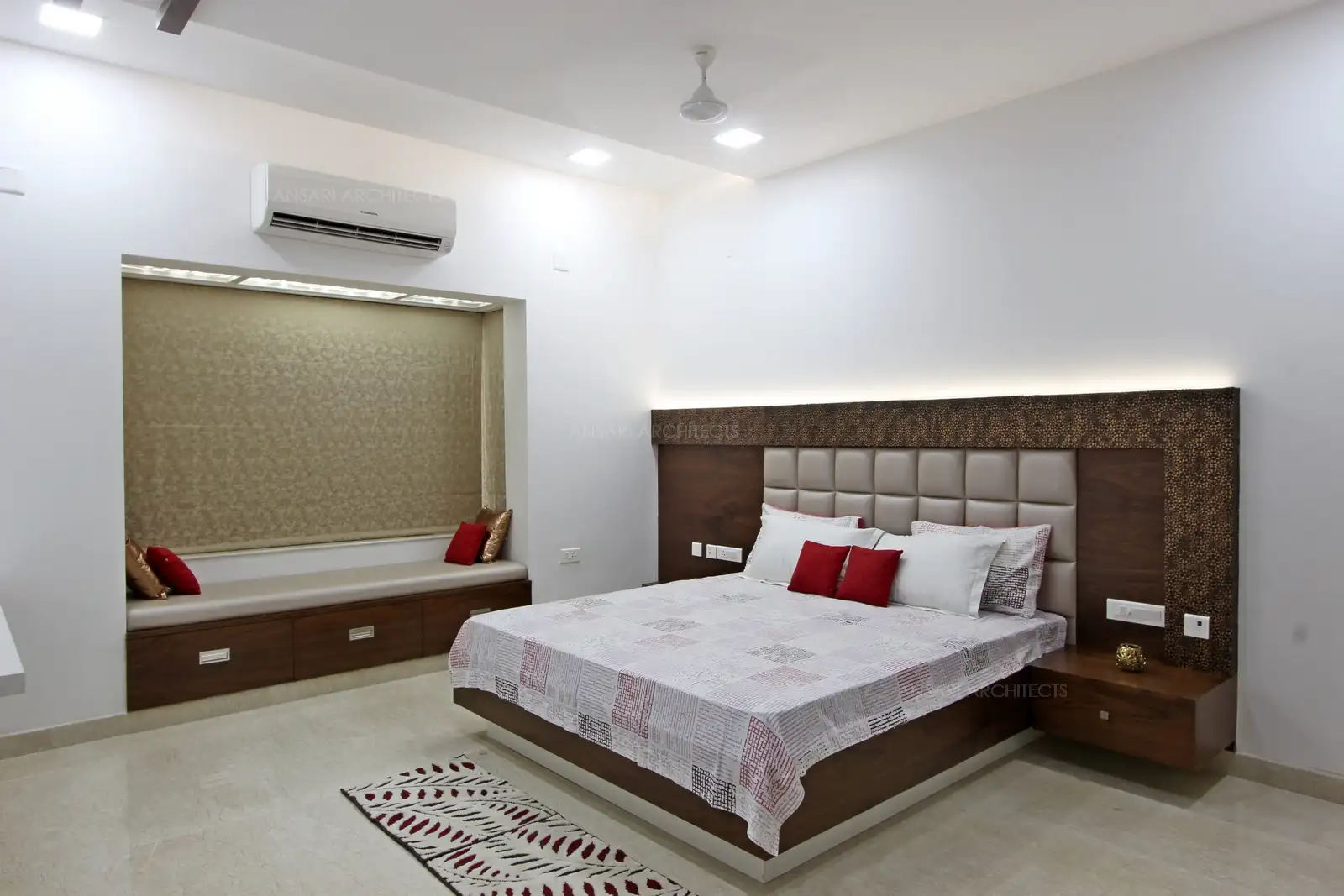 Cloaked in Alabaster tones, this bedroom is a vision in white. The muted panel offer visual variety to the expanse of neutral colours. A red patterned area rug anchors the sleeping zone while clear sitting windows bathe the room in natural light. The bedroom space brims with character.