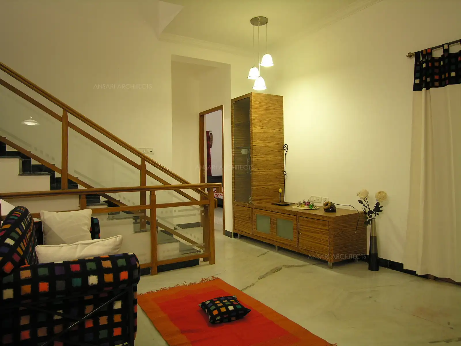 Family room in the first floor has bright multi colour furnitures with simple display unit highlighted with hanging lights in the landing area.