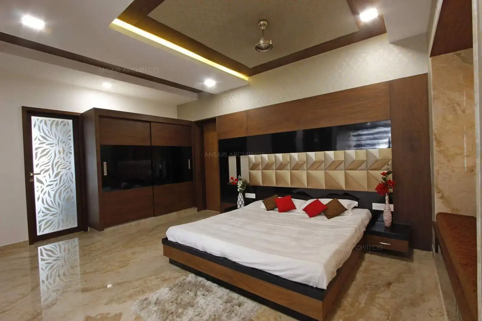 The well-spaced in spectrum of decor schemes with contemporary luxe bedroom. The wall featured behind the bed, is a single expanse of veneer panelling offering a clean vibe with neutral shades in the headborad. The cove lights emphasize the design and depth of the false ceiling.