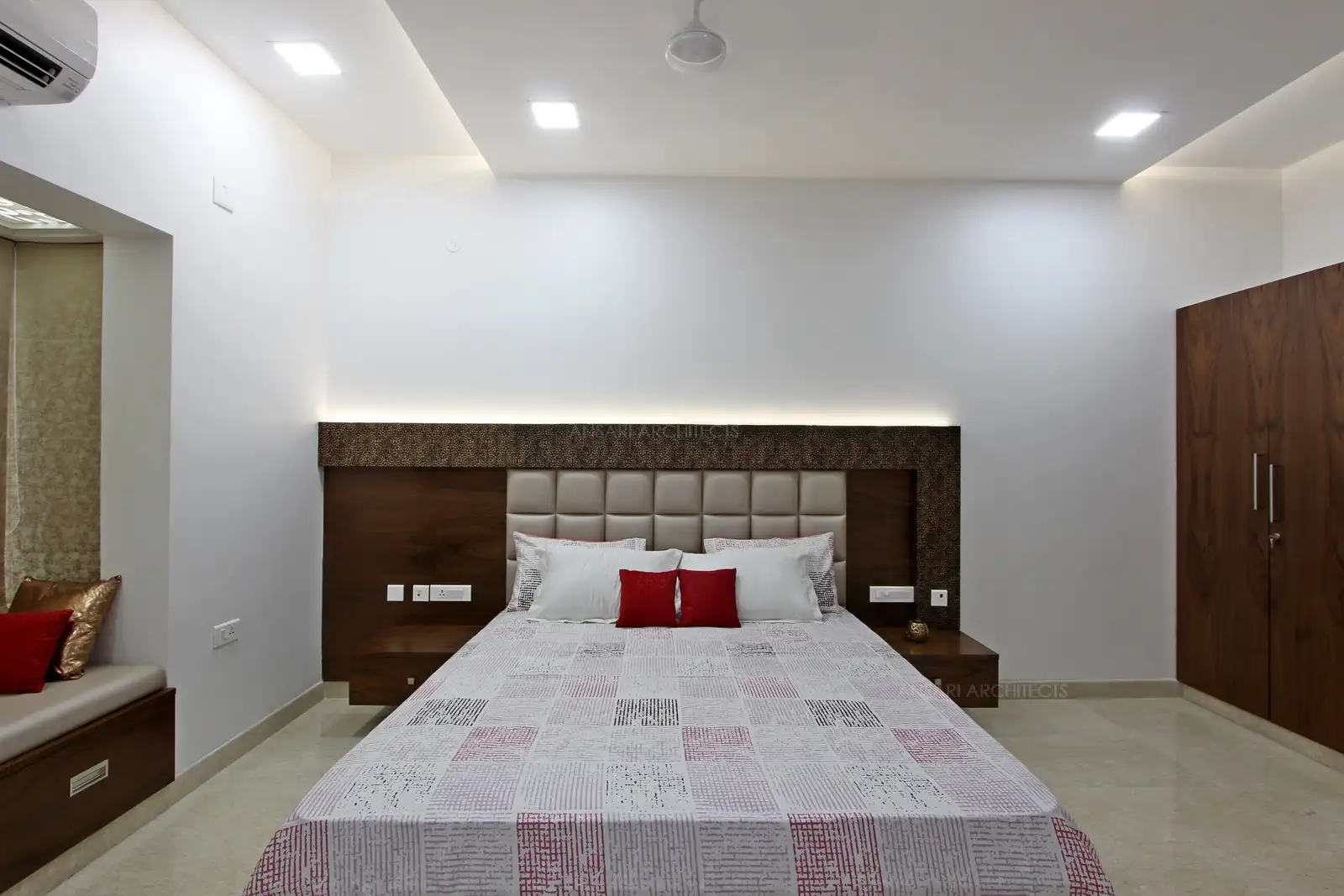 Recessed lighting carpets the room in soft light. Sitting window in golden accent seating add pops of colour to the aesthetics. The centred headboard is baklit with striplights and acts as an unapologetic emblem of the bedroom with eye-popping decorcushion and bursts at the seams with golden lining.