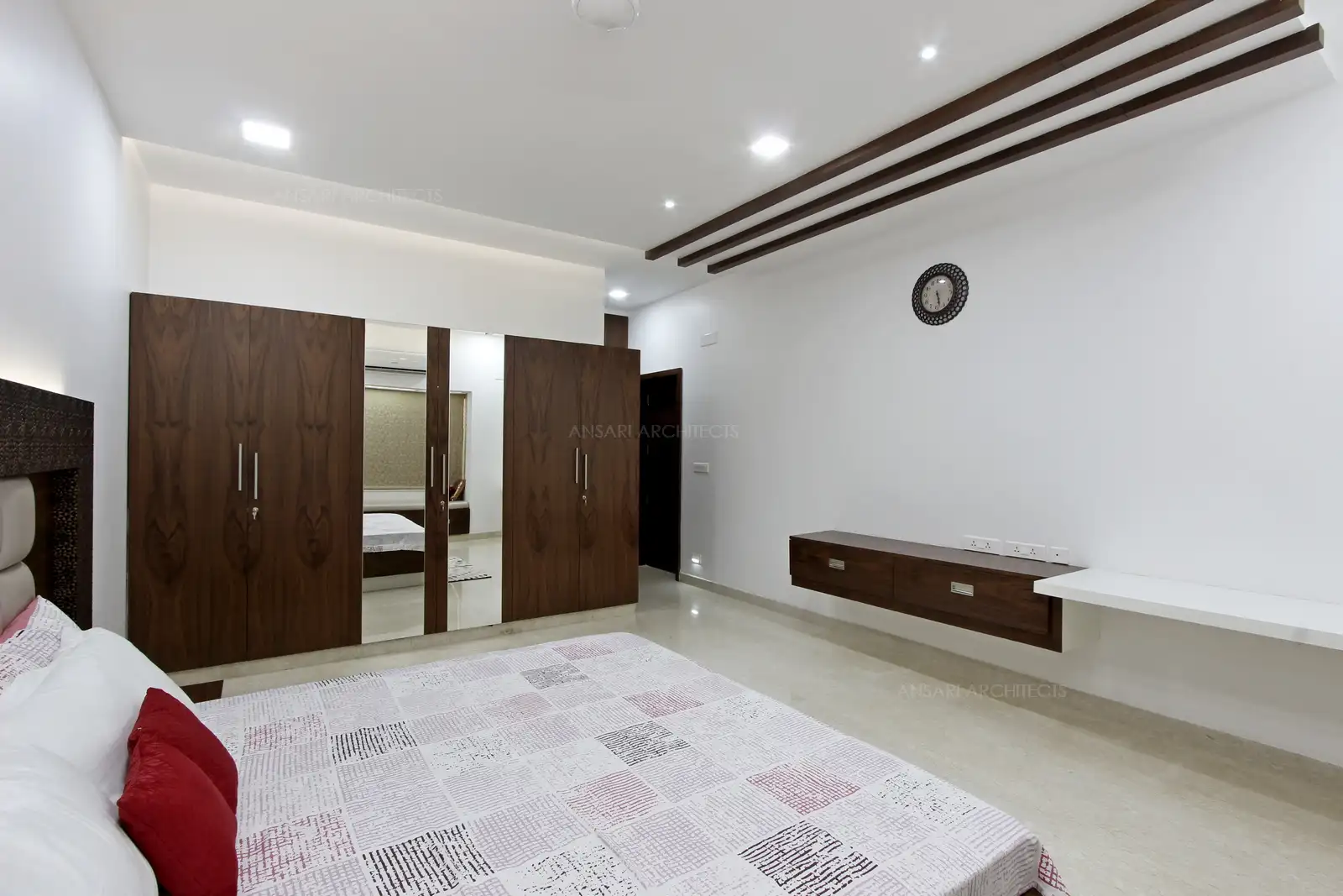The wood panelled wardrobe enriches the room with a subdued elegance, with functional study table exuding luxury with wood strips in the ceiling. The white walls complement the furnishings and vanity.