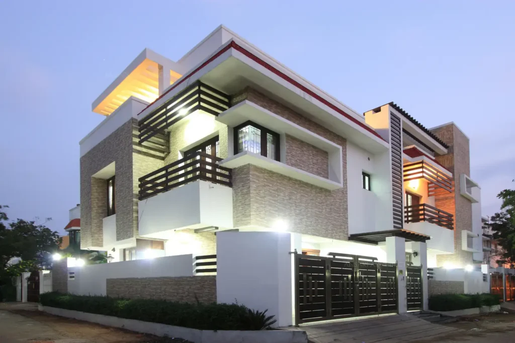 Modern two-story house at dusk, featuring contemporary architecture with a stone facade, wooden accents, and illuminated balconies, set in a suburban neighborhood.