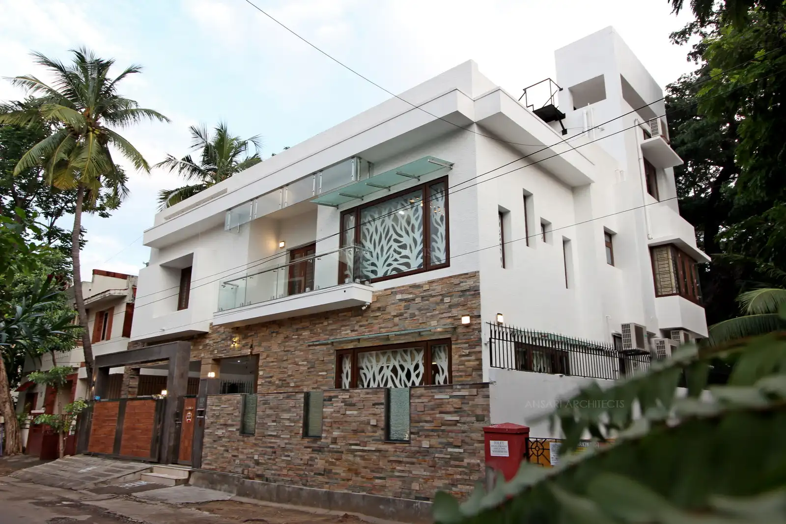 Glass ensures a sense of lightness in the all-white building and creates a subtle contrast in the exterior between stone cladding and the white backdrop of the building. The element in the entry with stone cladding creates a bold statement and breaks the monotony of the all-white exterior.