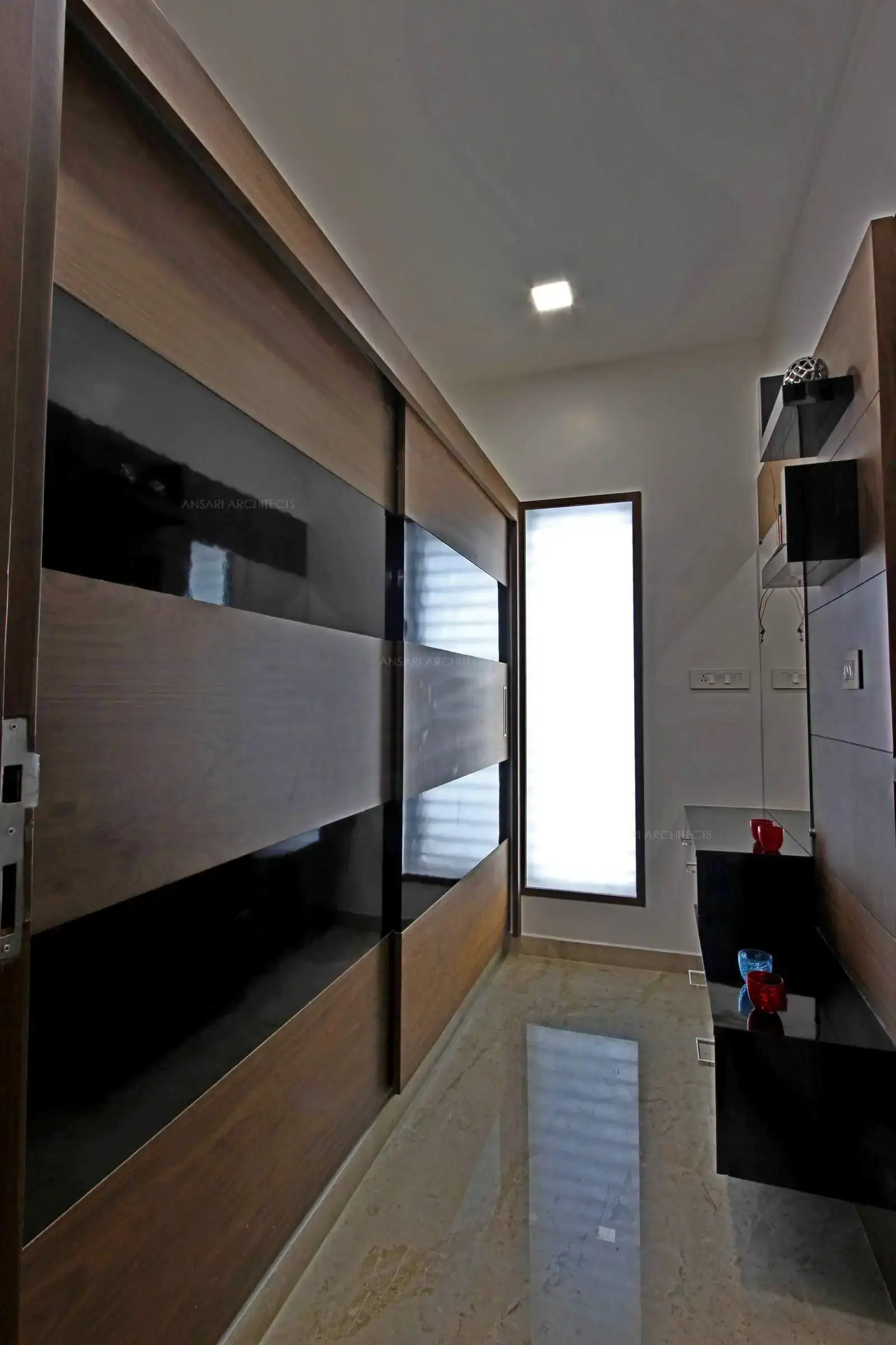 The panelling lends an opulent touch with neutral black. Marble flooring breaks the monotony of the bedroom. The wall is wood clad along with the functional table design adds visual richness.