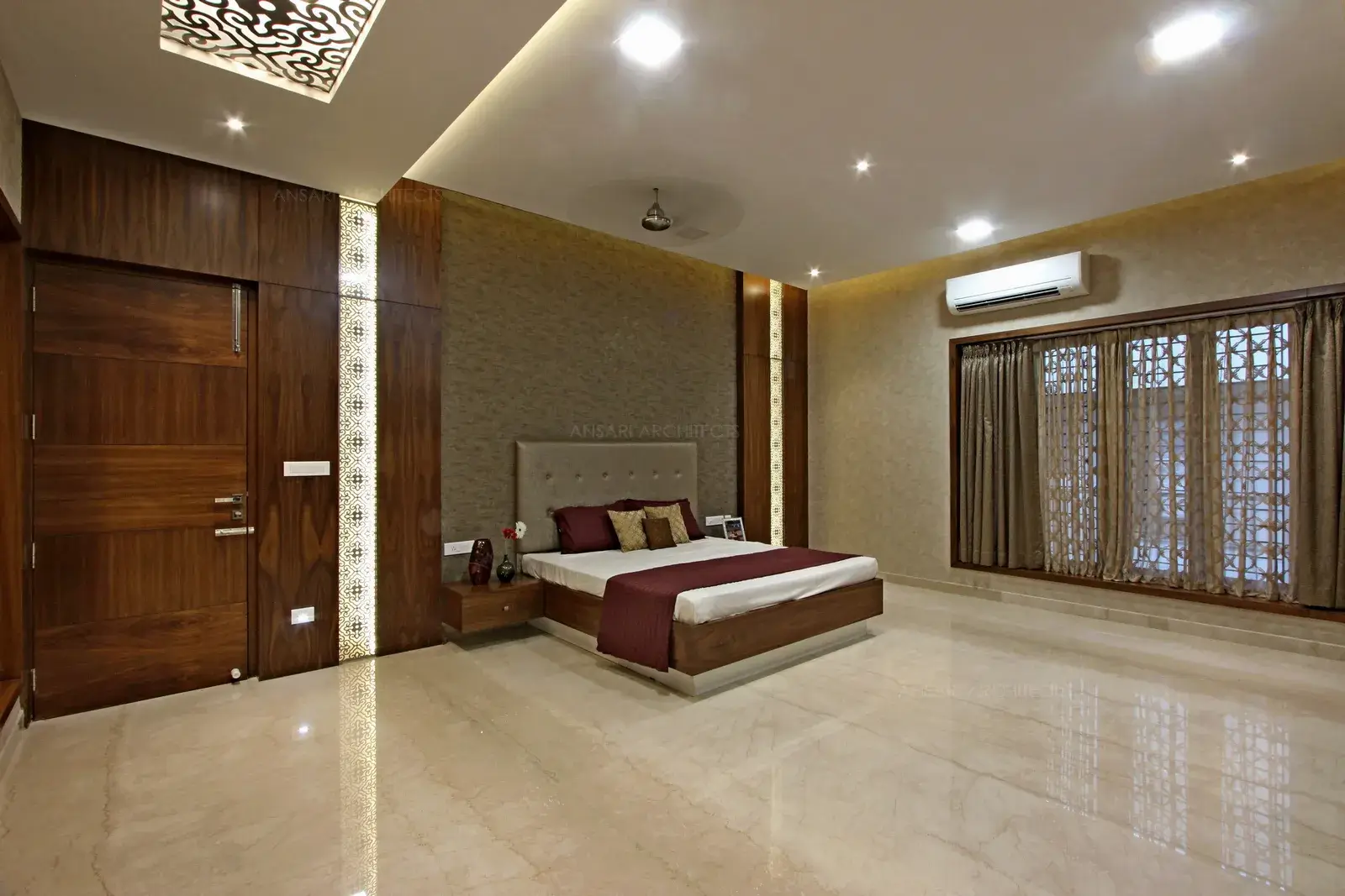 A wallpaper accent wall, framed by three way brown wood peninsula acts as an arresting focal point. The wooden panelling depicts luxury. The muted panel walls offer variety, french windows bathe the room in natural light. The space brims with character and classical wall with golden detailing , gauzy curtains enveloping the sleeping area. Recessed lights hosted in the ceiling looks majestic.