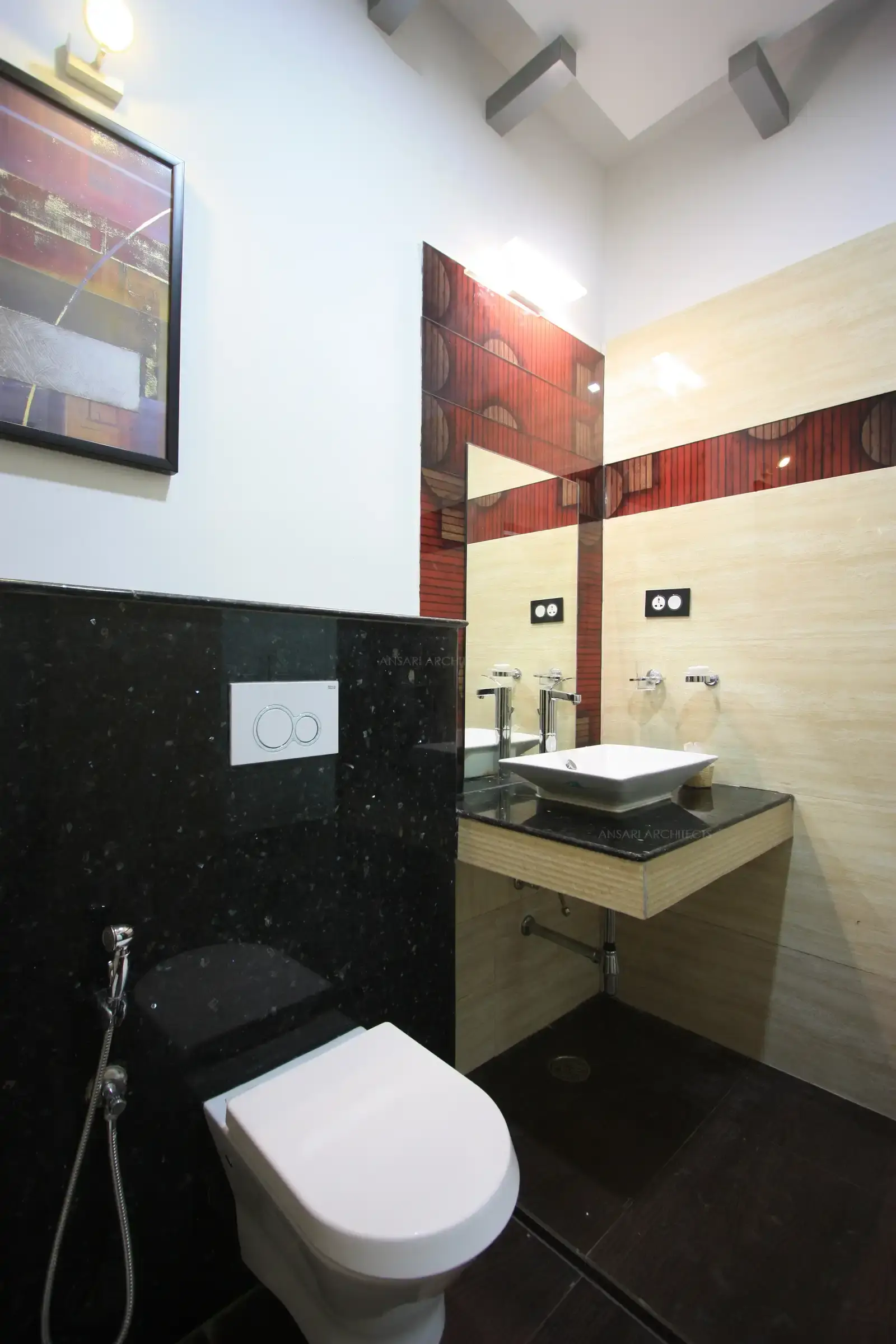 The toilet has contrast red colour tiles against beige and black granite finishes.