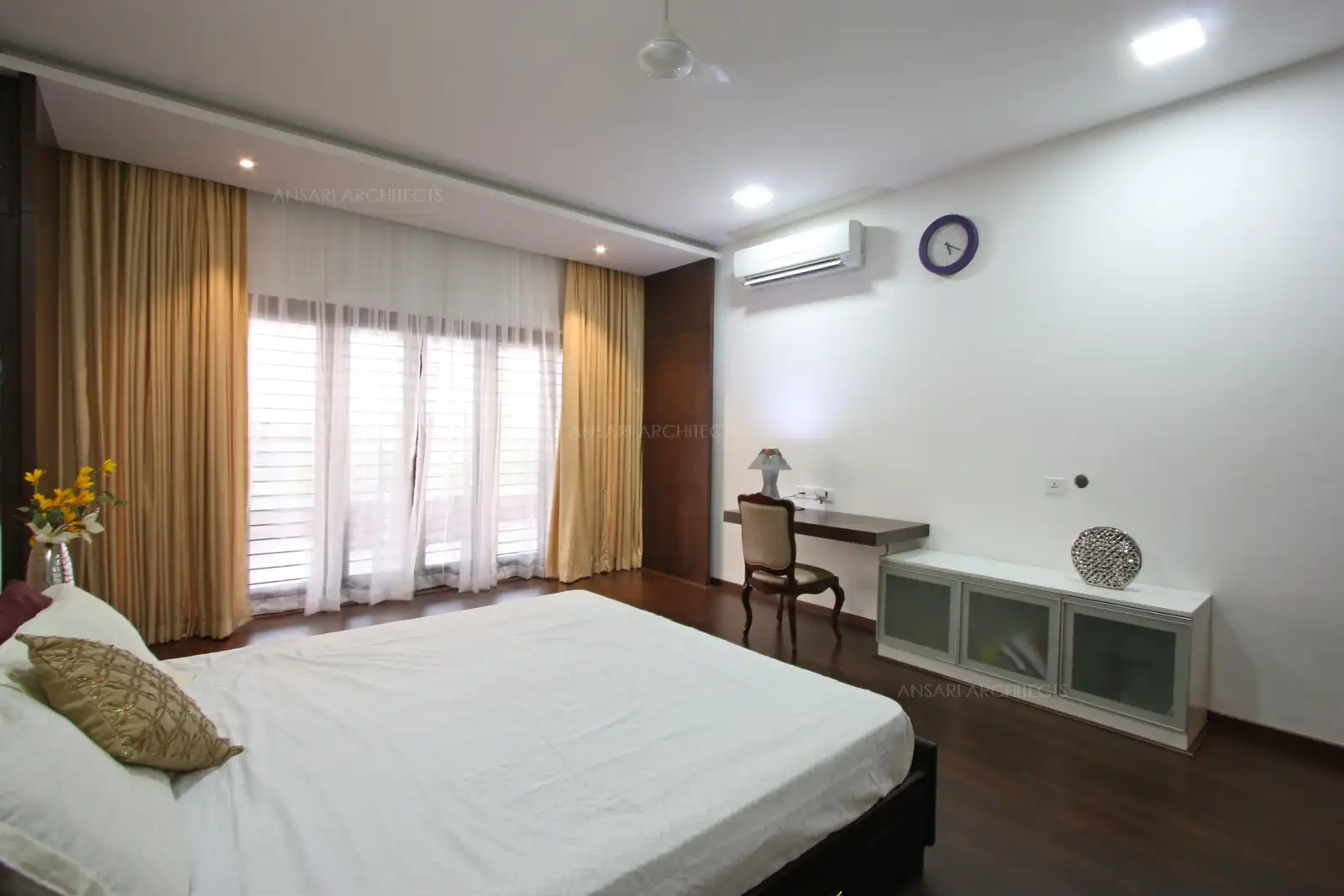 The bedroom with wooden flooring creates a warm feel, functional glass bookcase also acts as a table, wood panels add in a rustic touch to the space, with a study area comfortable with ample lighting to avoid glare.