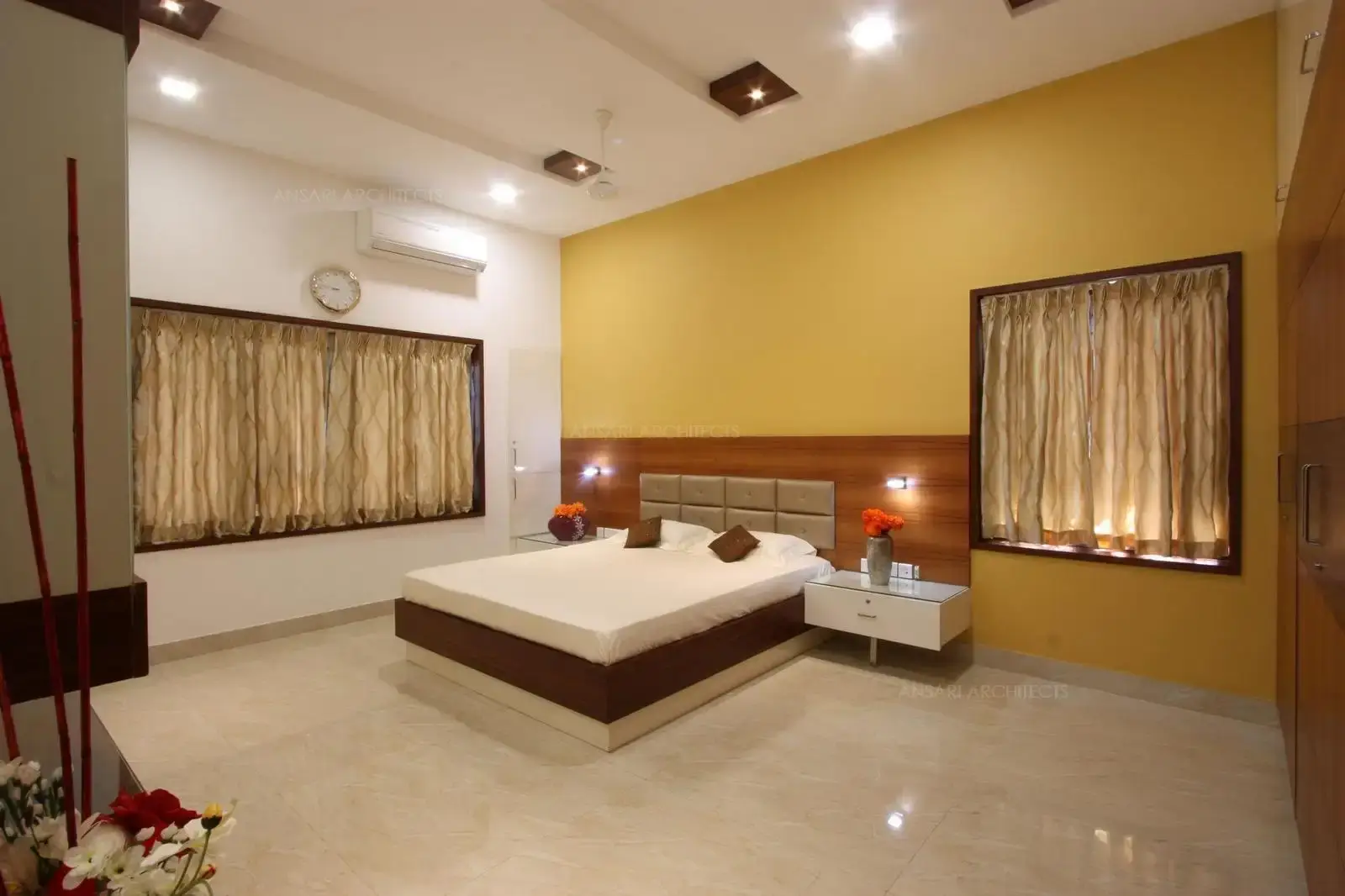 The bedroom is a modern, simple and spacious area which repletes with custom furnitures and lighting. This bedroom shows a room lush witha soft yellow that adds depth to the overall palette. The white walls breaks up potentially, the headboard seems to be overwhelming with embossed cushion and lights on either sides.