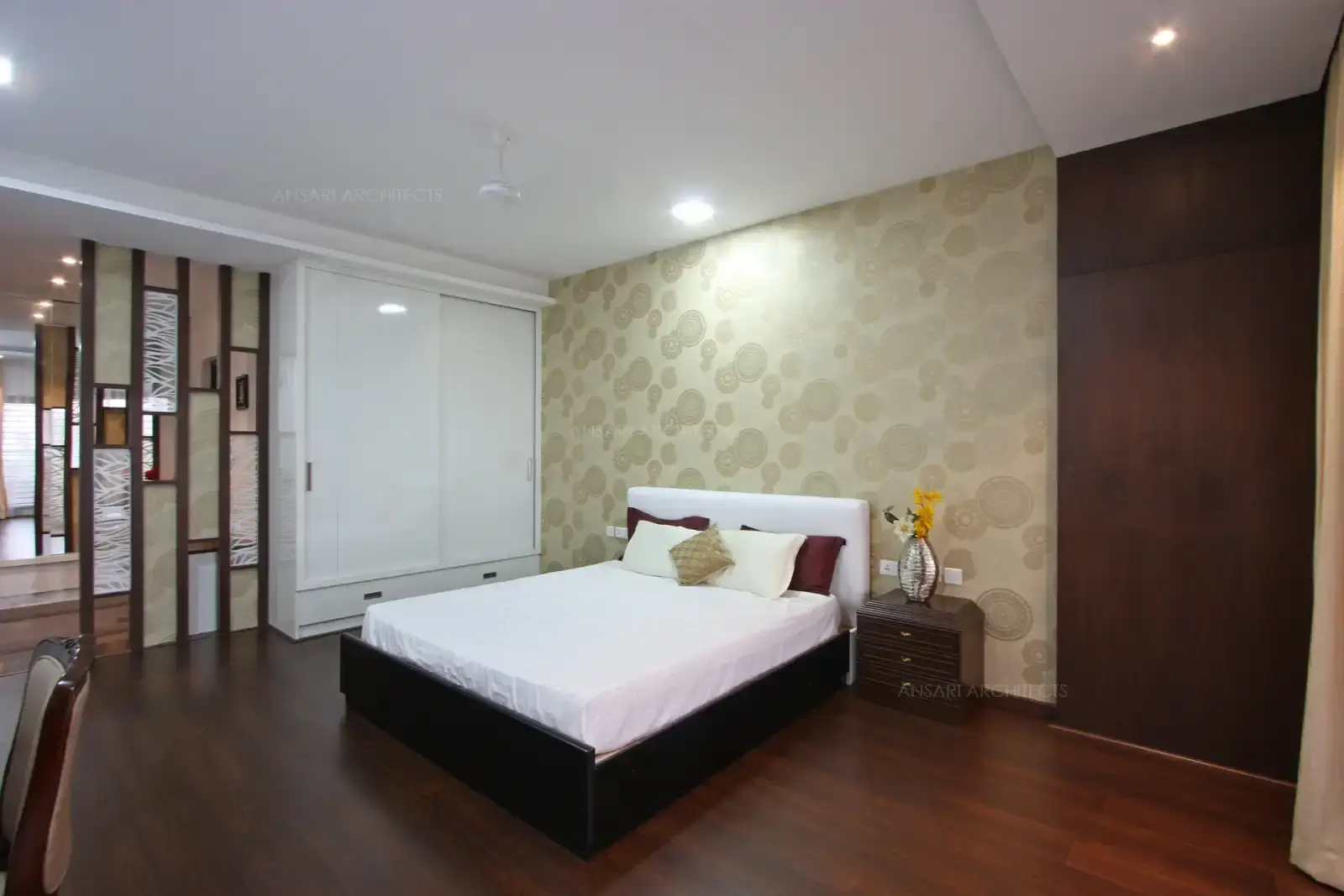 The feature wall covered with stunning wallpaper, white cushioned headboard, the wardrobe camouflages with the bedroom smooth white walls, the partition wall adds a loads of elegance to the room with frosted pattern glass.