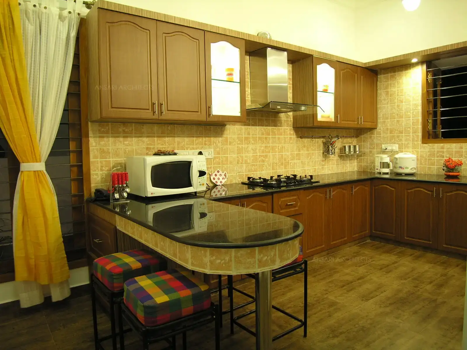 Neutral colour scheme has been broken with multi colour fabric given in seating of breakfast table in this spacious kitchen.