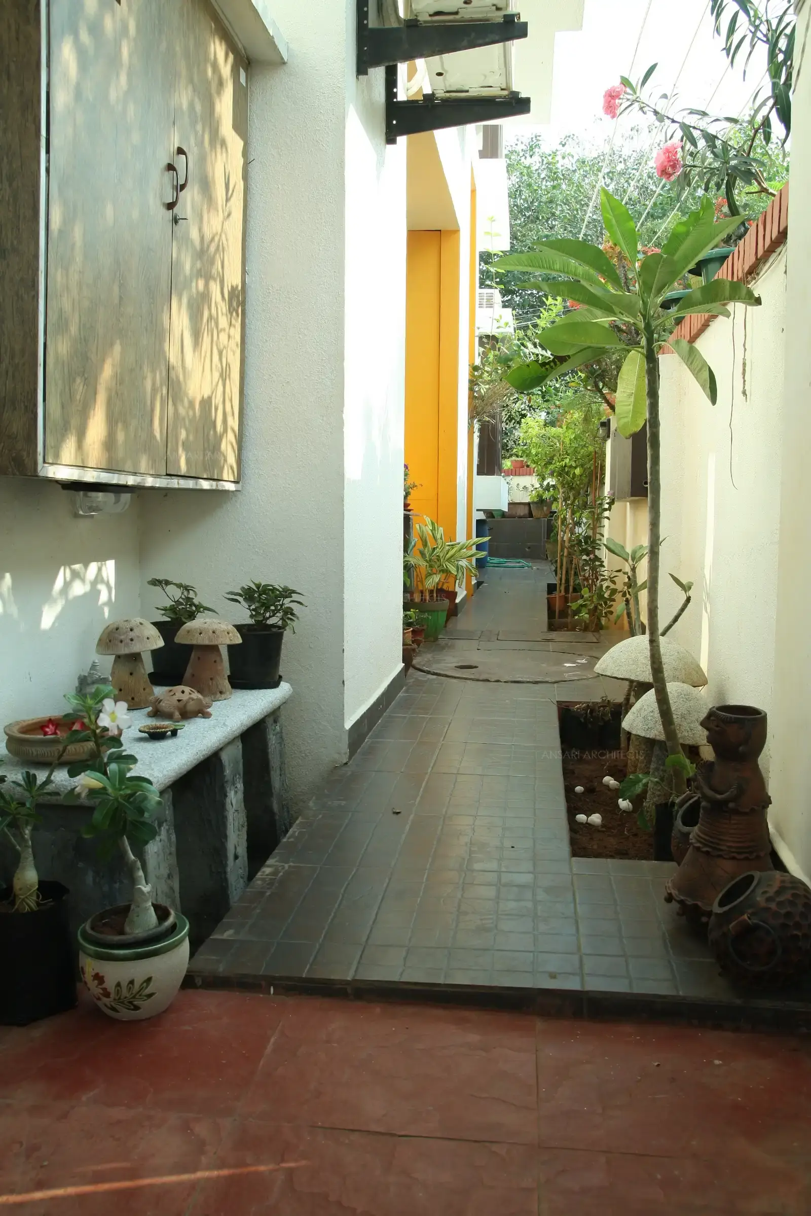 The passage around the house has been designed in rustic plain flooring with planters with Terracotta and stone murals