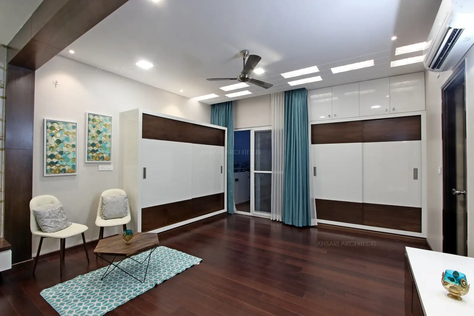 The backlighting infuses a dramatic effect, the mellow colour combination for the bedroom imparts a dynamic look, and highlights the wardrobe unit which camouflages with the wall and dark veneer strips bring in contrast.