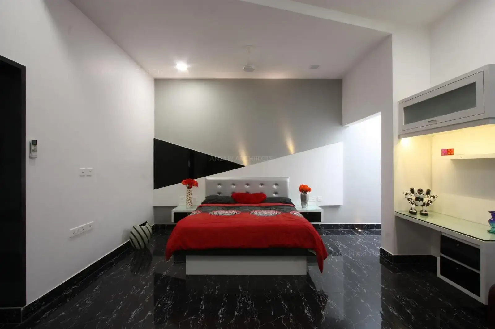 The harmony among the neutral colours is achieved by the headboard shades with wall lighting. The deeper shades of red in the bedding and floating bedsite unit is electic. The flooring contrasts the walls and provides a vibrant effect .