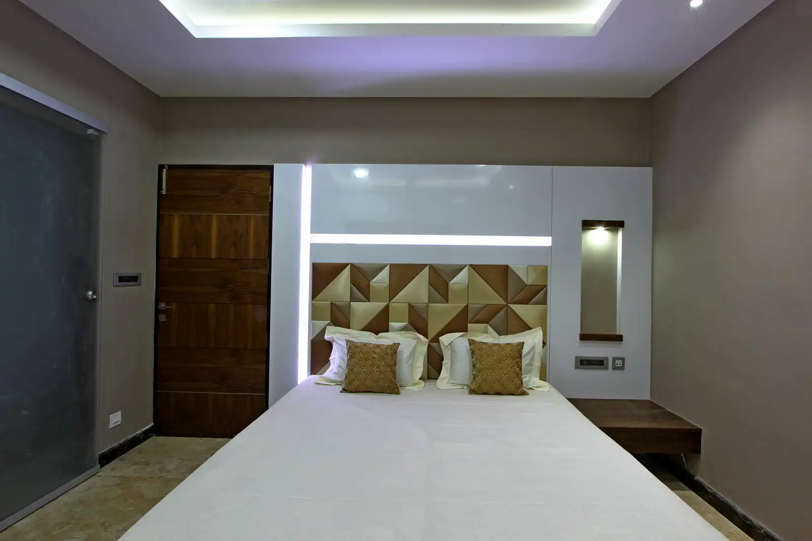 The white panelling with strip light provides visual relief and with a sleek side table along with a mirror .The brown and beige headboard with patterns create a elegant space.