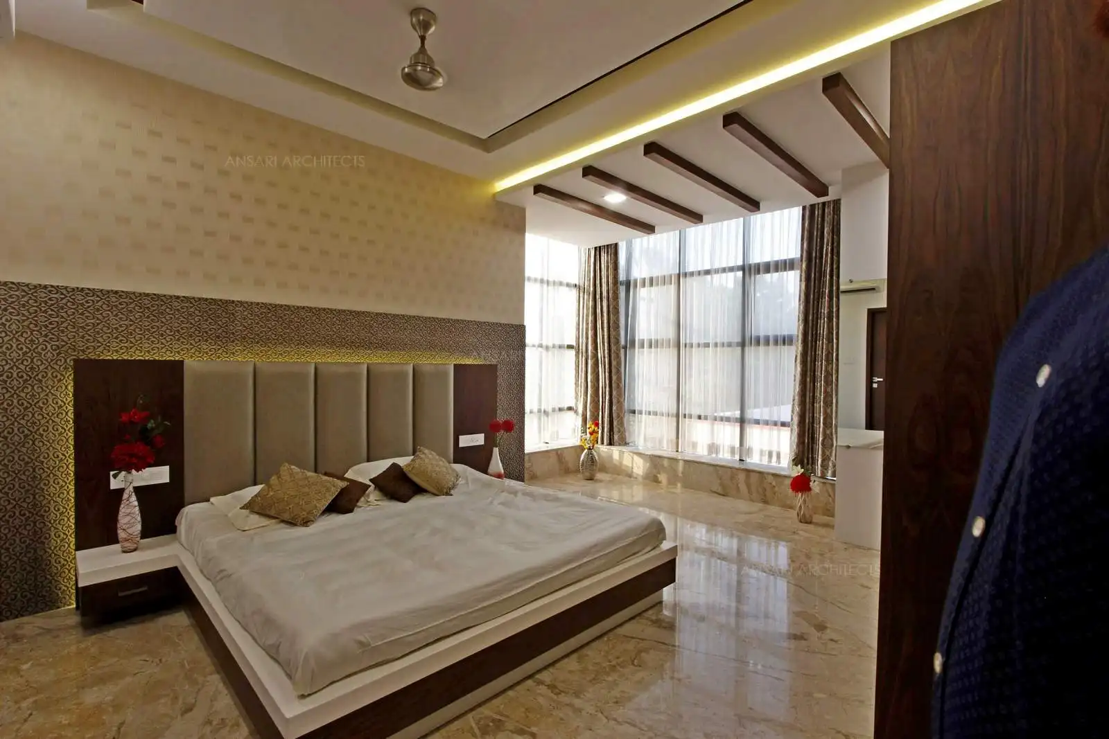 The corner window takes it place whilst the headboard is designed with all parts of royalty the golden outline offers a lustre along with the veneer panel, the embroidered cushion embossed entirely using strip lights has a subdued elegance . The marble flooring enriches the room decor.